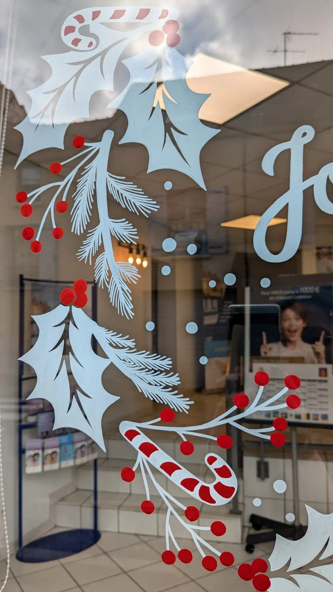 Peinture sur vitrine de Noël réalisée pour l'agence Aréas à Vaux sur-Seine (78). Détail sur le motif végétal composé de baies, de feuilles de houx et de branches de pin. Coloris rouge et blanc