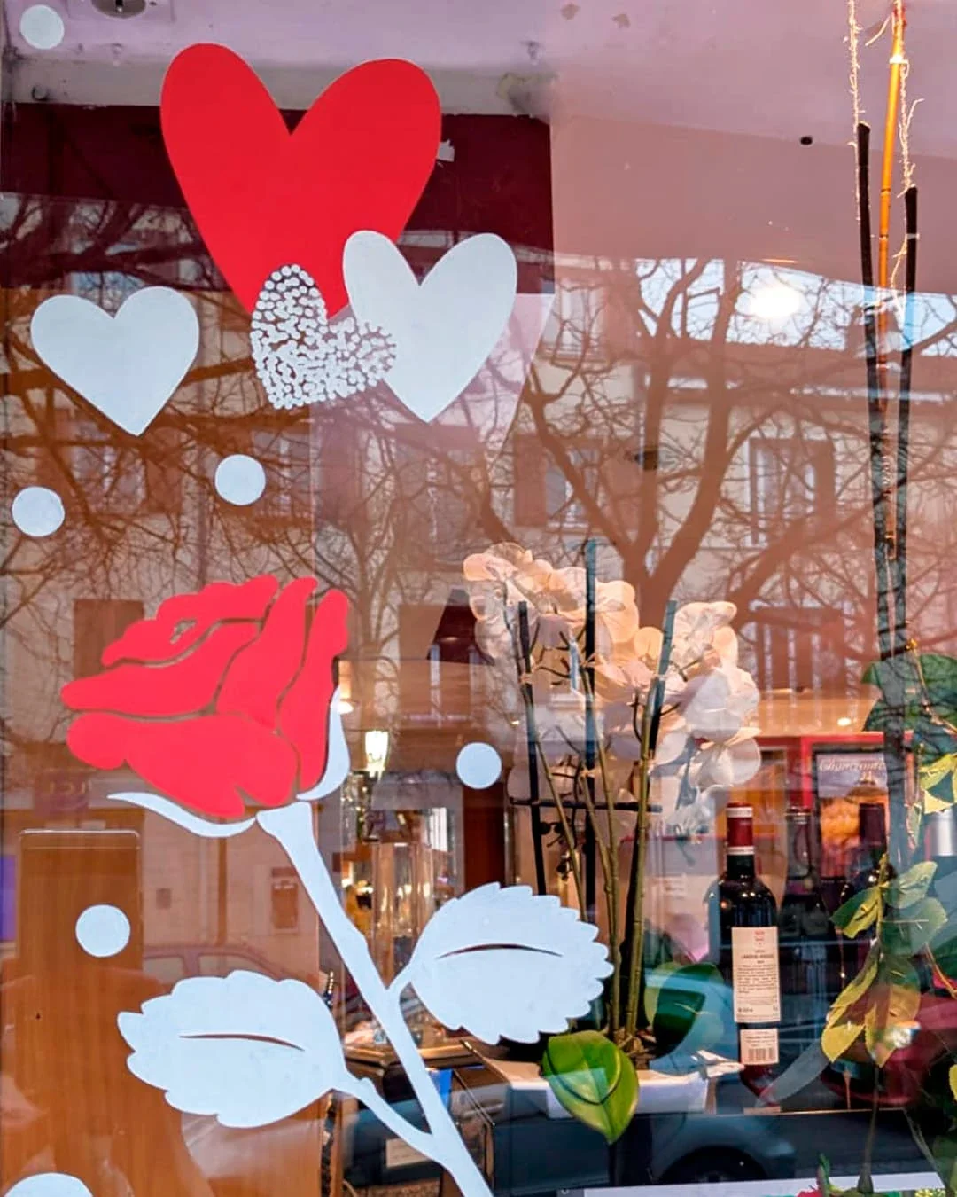 Peinture sur vitrine, thématique Saint-Valentin. Gros plan sur le motif de la frise décorative avec des roses et des cœurs. Coloris rouge et blanc.. Traiteur à Croissy-sur-Seine (78)
