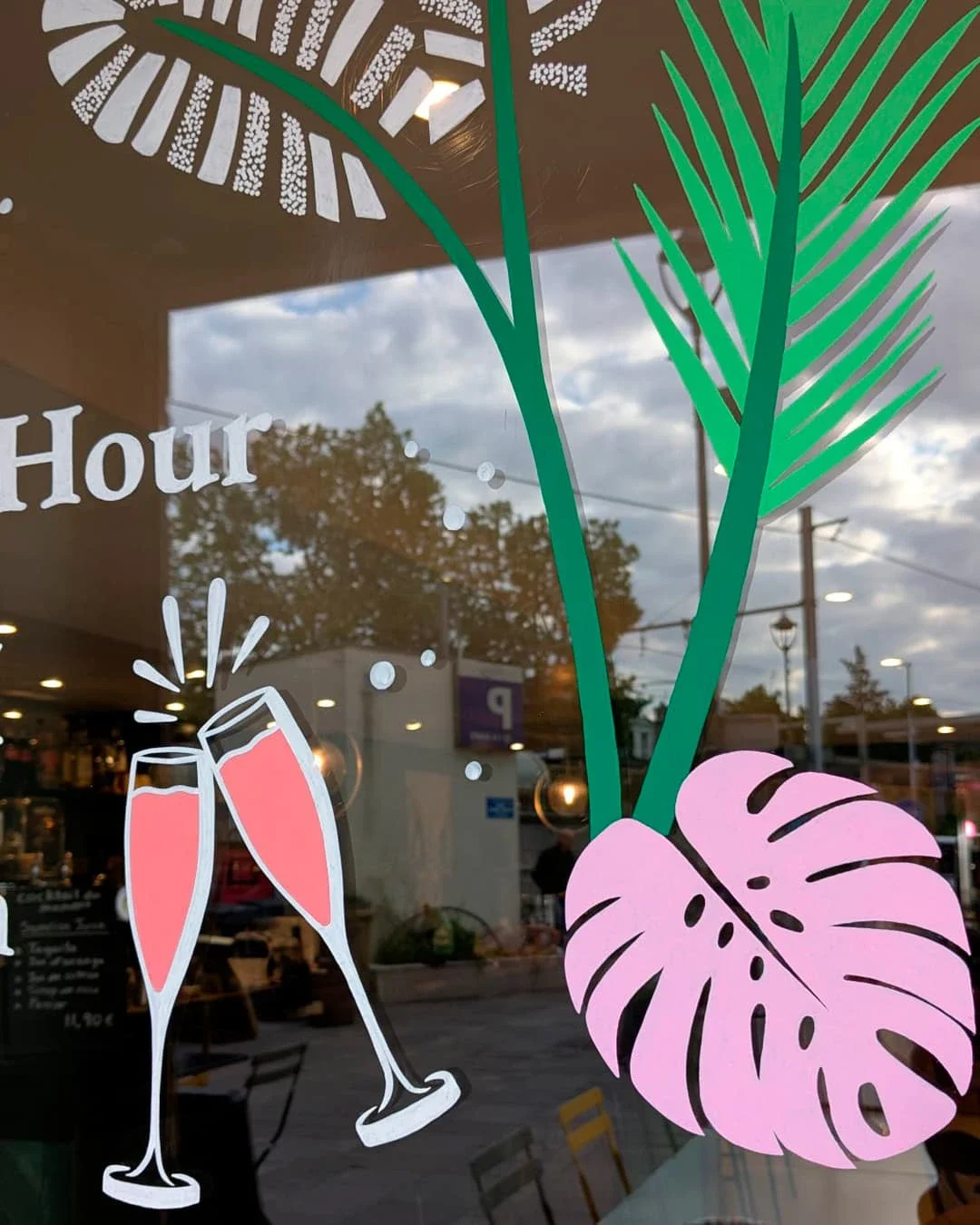 Peinture sur vitrine, sur-mesure, bistrot papillote Chatou (78). Thématique jungle bohème, coloris blancs, verts et roses. Gros plan sur les coupes de champagne