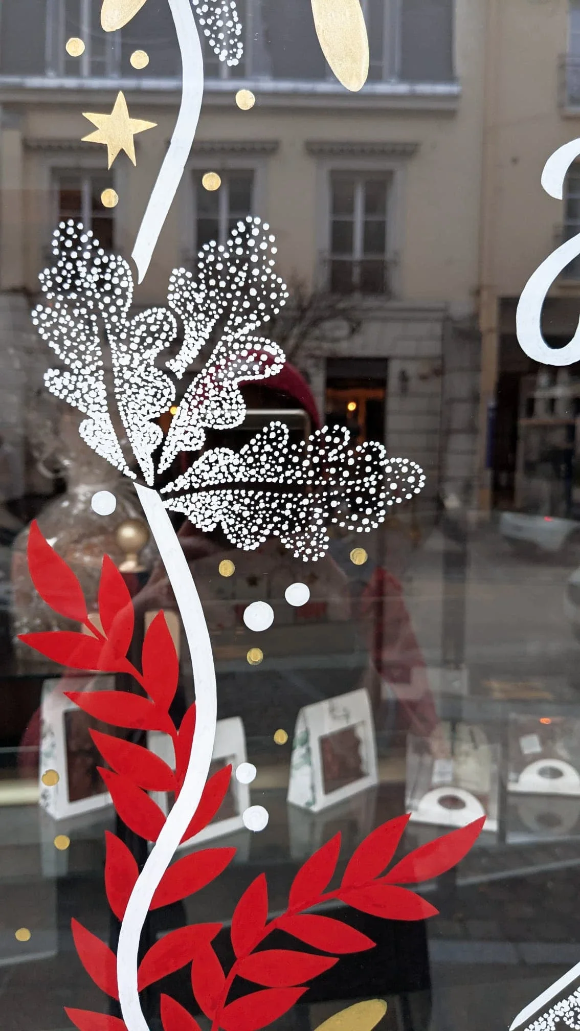 Détail de la frise végétale peinte à la main avec feuilles de chêne, baies rouges, étoiles et ruban sur une vitrine de Noël pour la boulangerie Duhamel à Saint-Germain-en-Laye