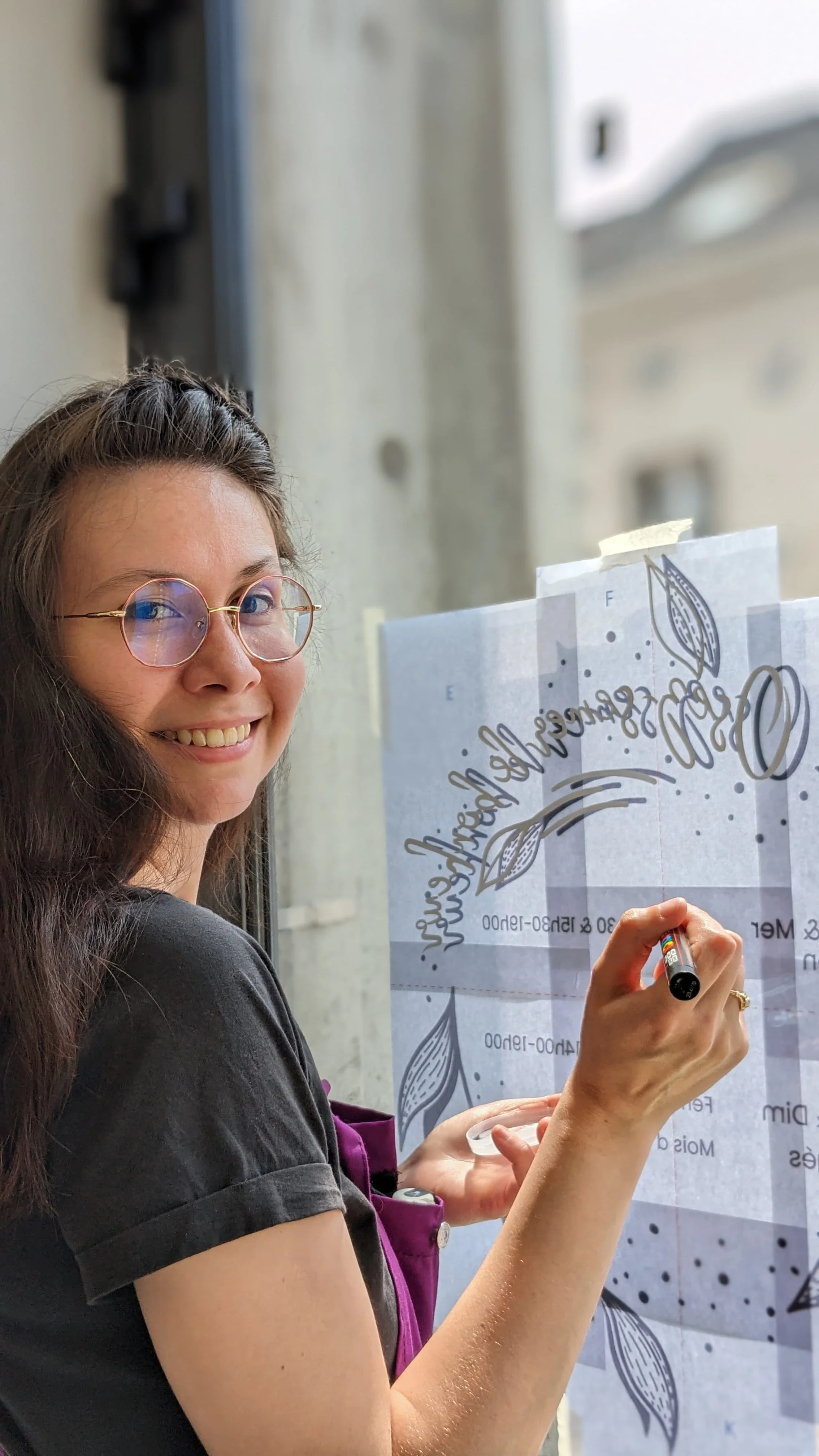 Illustratrice spécialisée en peinture sur vitrine, création d'une couronne d'horaires peinte à la main à Vaux-sur-Seine (78) en prestation en train de peindre une couronne d'horaires