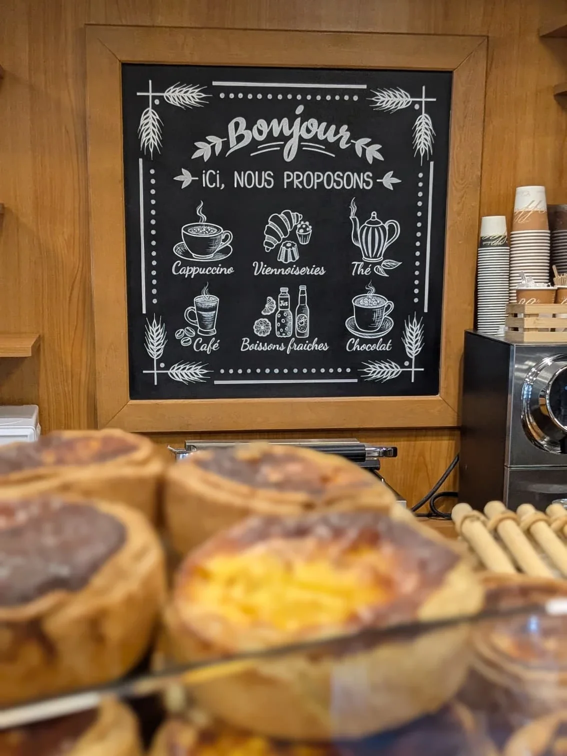 Ardoise murale peinte à la main pour une boulangerie à Saint-Germain-en-laye (78). Lettrages et éléments peint en blanc pour communiquer sur l'offre de boissons à emporter. L'ardoise est accrochée derrière le comptoir à pâtisseries.