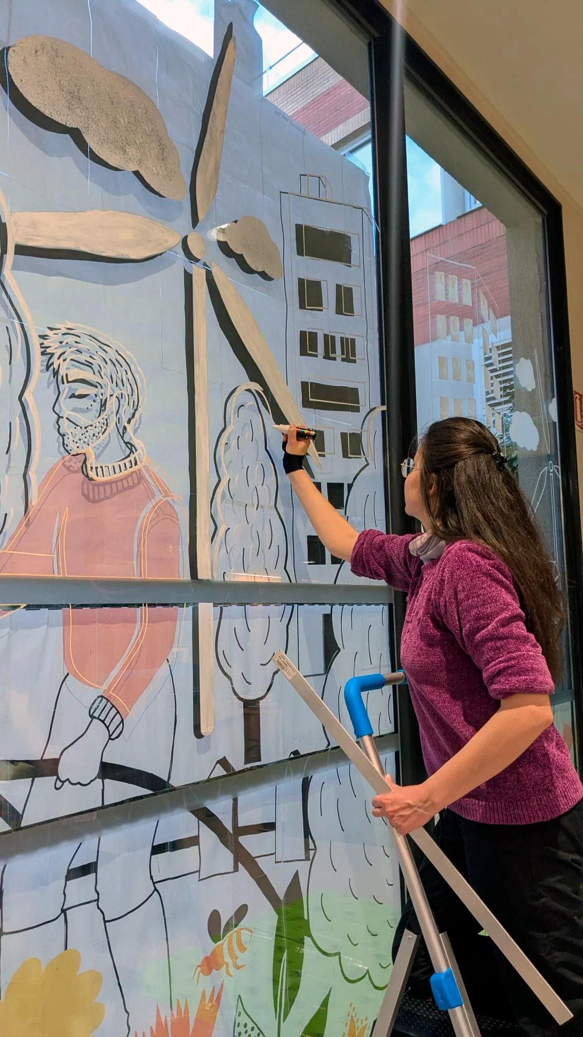 Fresque participative sur les vitrines du patio de la médiathèque des Mureaux, réalisée lors des Nuits de la lecture 2026. Thème "Villes et campagnes" — L'illustratrice Sandrine Daniel réalise le travail préparatoire avant l'arrivée du public