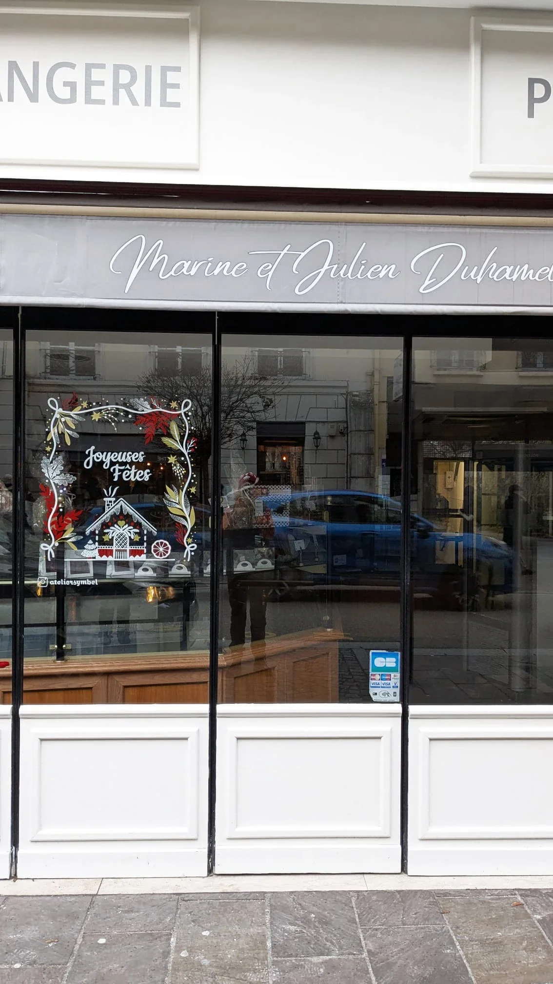 Façade de la boulangerie Duhamel à Saint-Germain-en-Laye décorée d'une peinture de Noël réalisée à la main avec frise végétale, lettrage « Joyeuses fêtes » et maison de pain d'épices