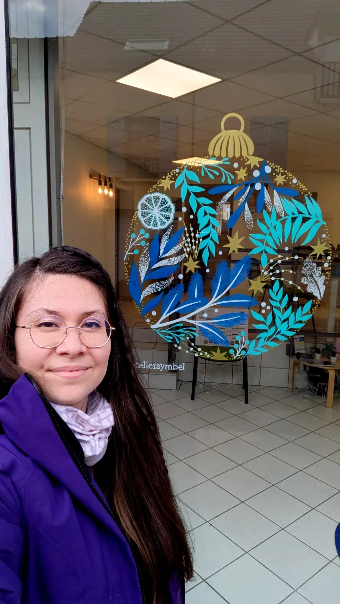L'illustratrice et peintre Sandrine Daniel à côté de sa peinture sur vitrine de Noël pour l'agence d'assurances Areas à Vaux-sur-Seine représentant une boule de Noël