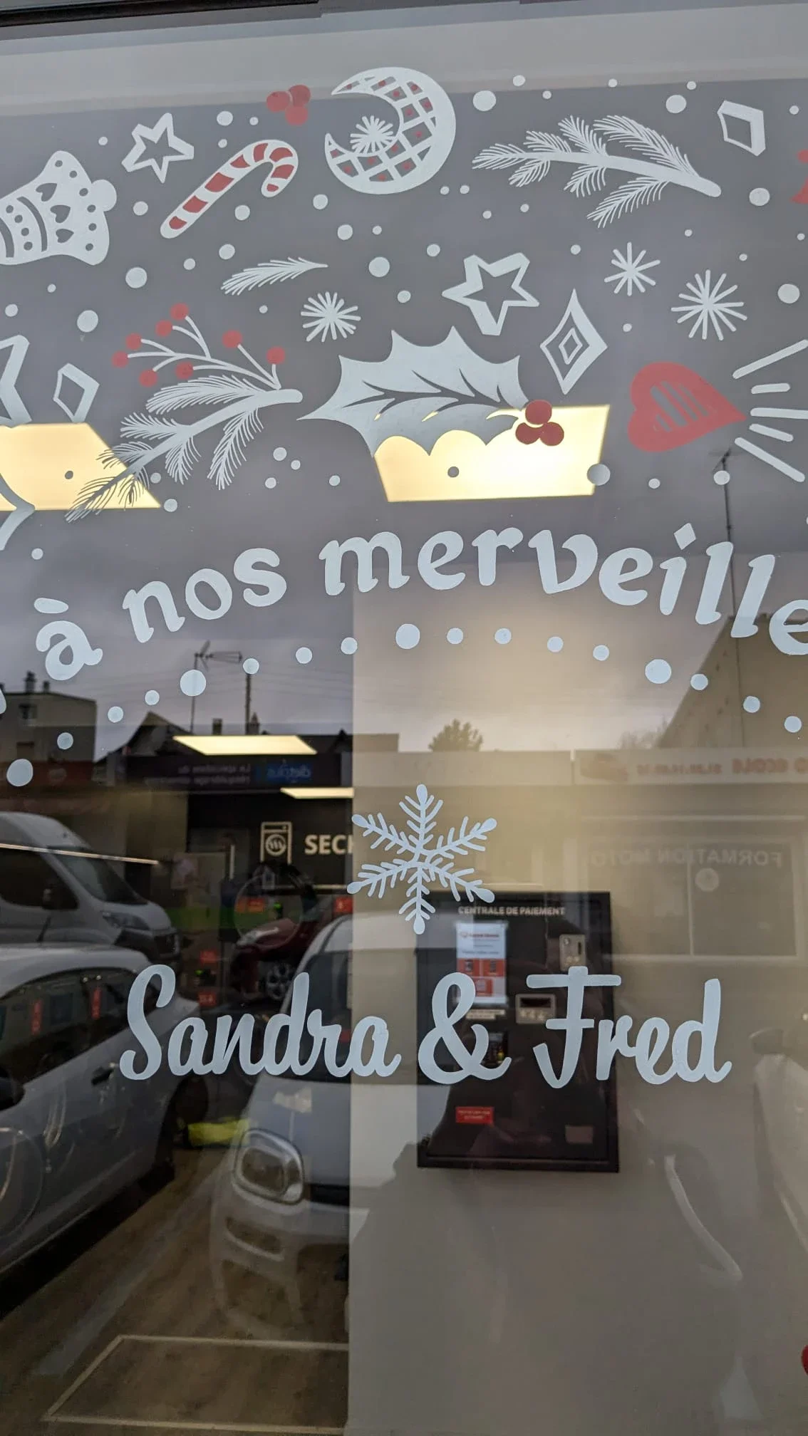 Gros plan sur le lettrage peint à la main « Merci à nos merveilleux clients » au cœur d'une décoration de Noël sur la vitrine d'une laverie.