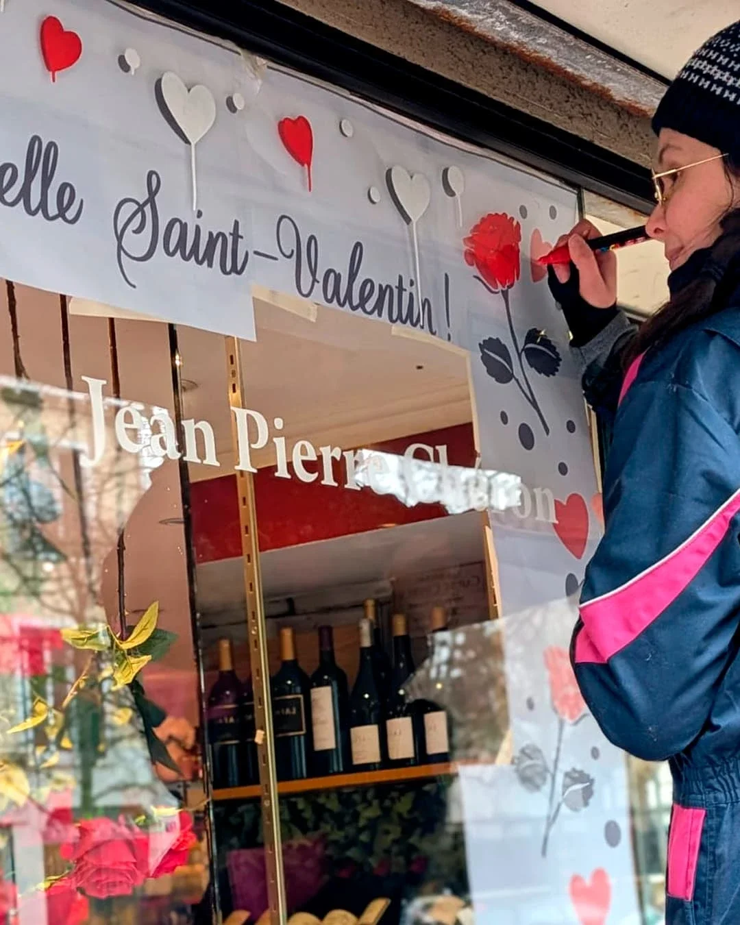 Peinture sur vitrine, thématique Saint-Valentin. Peinture en cours de la vitrine de gauche. Frise décorative avec des roses et des cœurs. Coloris rouge et blanc.. Traiteur à Croissy-sur-Seine (78)