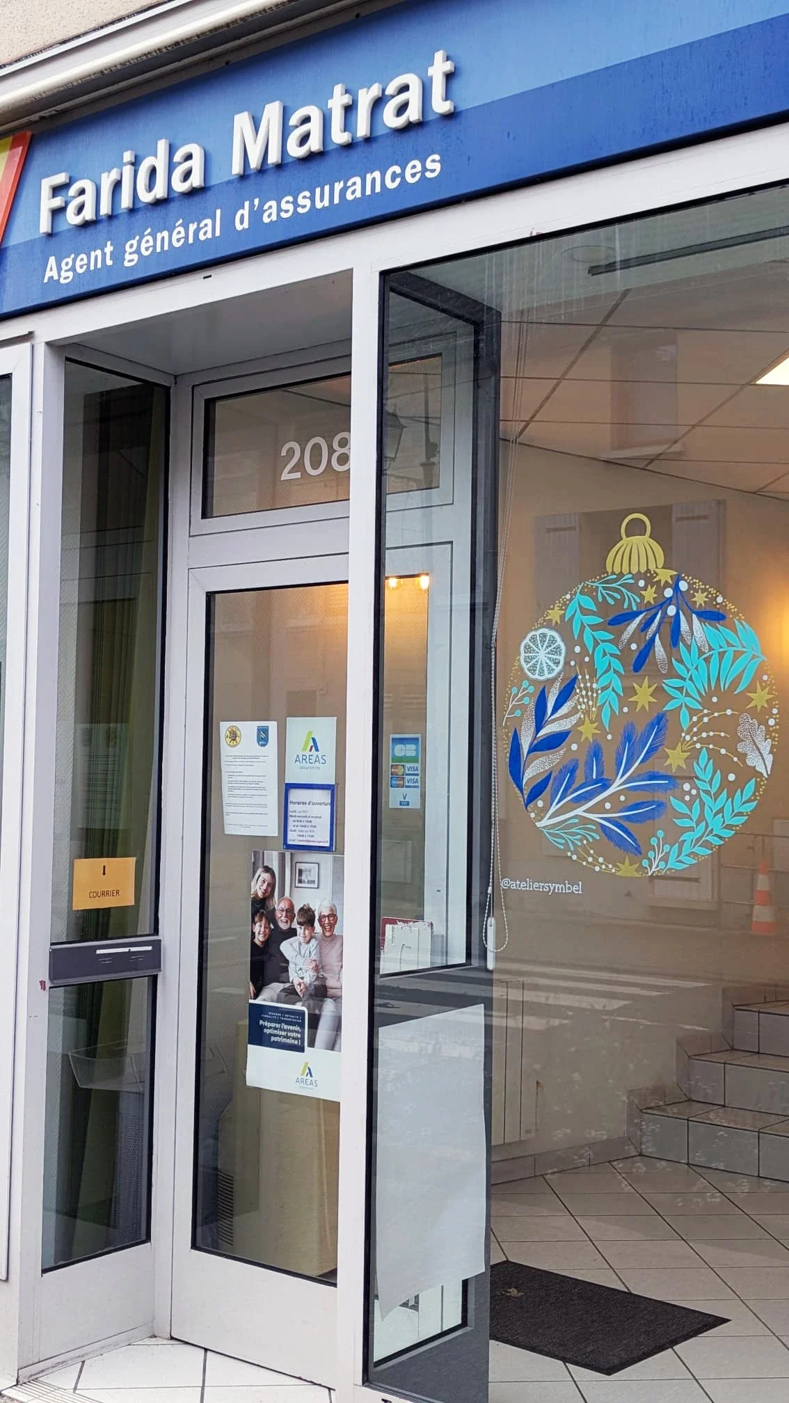 Façade de l'agence d'assurances Aréas Farida Matrat à Vaux-sur-Seine décorée d'une peinture sur vitrine de Noël réalisée à la main avec une boule de Noël aux tons bleu et dorés, ornée de végétaux et d'une tranche d'agrume.