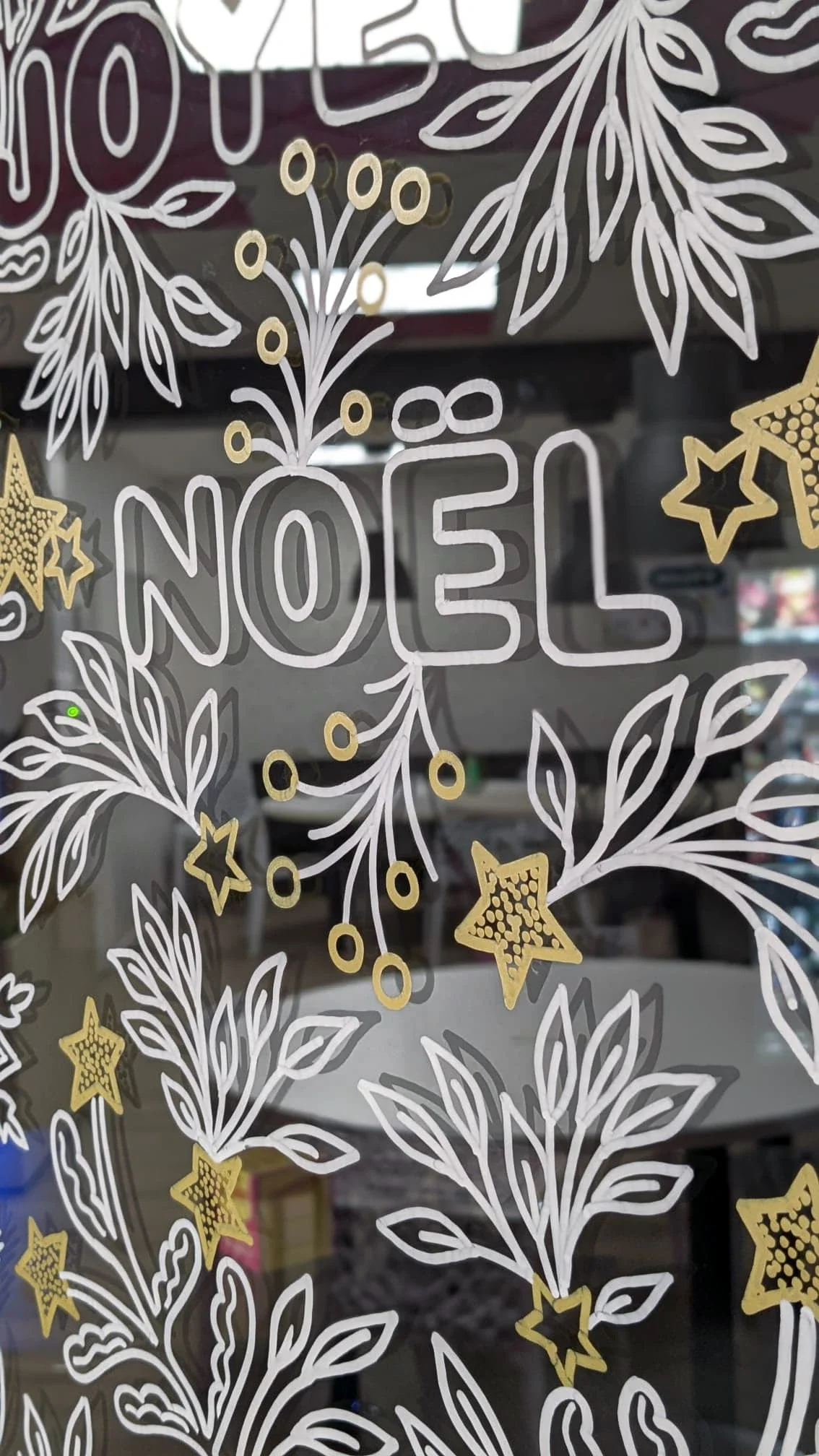 Détail du lettrage de Noël intégré à une frise végétale aux entrelacs blancs et dorés sur la vitrine du réfectoire