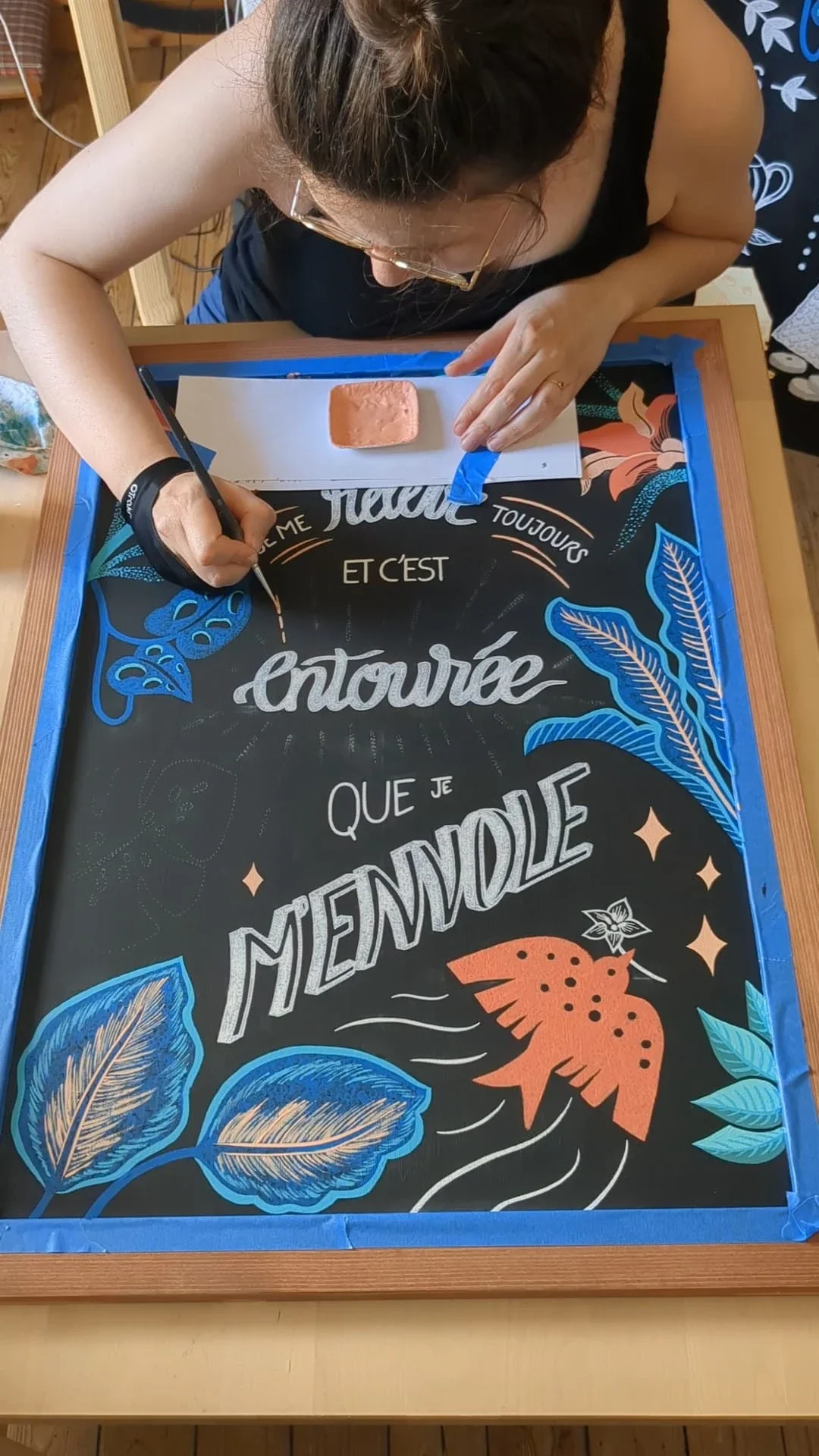 Réalisation de lignes pointillées décoratives autour du mot « entouré » sur une ardoise peinte à la main