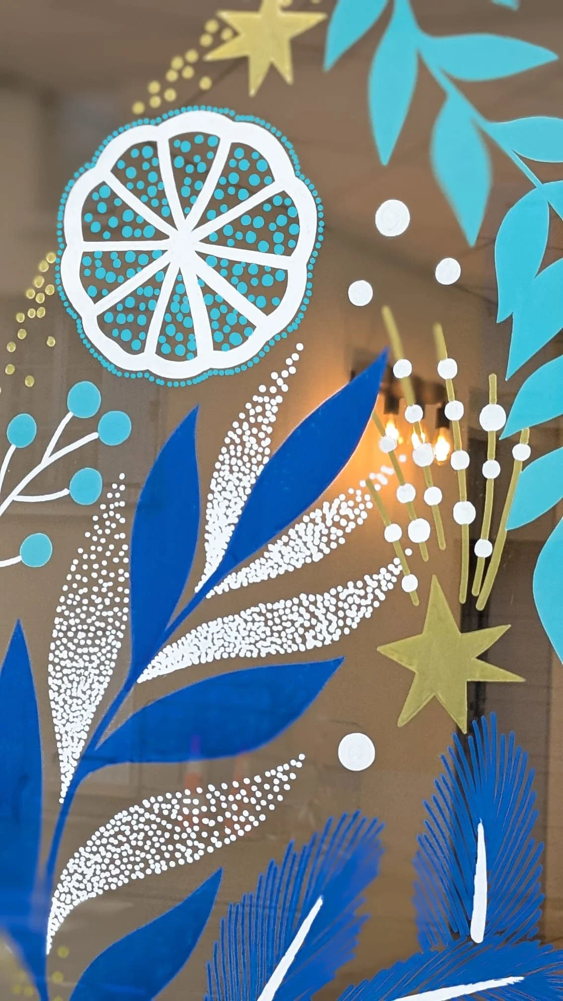 Gros plan sur la peinture sur vitrine de Noël, avec tranche d'agrume, étoile et végétaux, coloris blanc, bleus et doré