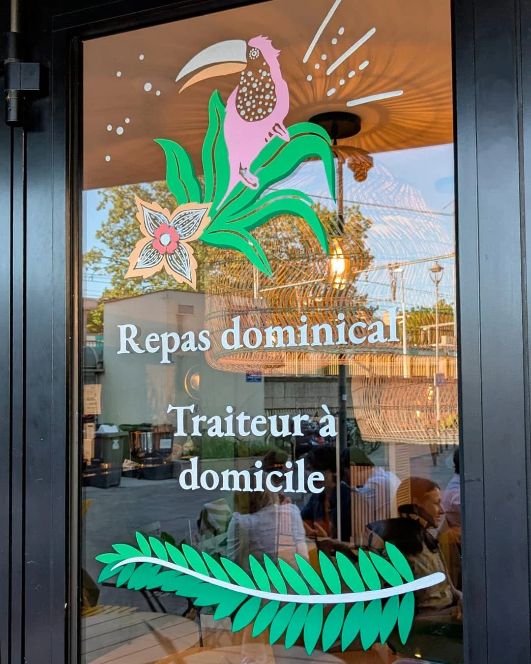 Peinture sur vitrine, sur-mesure, bistrot papillote Chatou (78). Thématique jungle bohème, coloris blancs, verts et roses. Oiseau, fleurs exotiques et végétaux, lettrage peint à la main.
