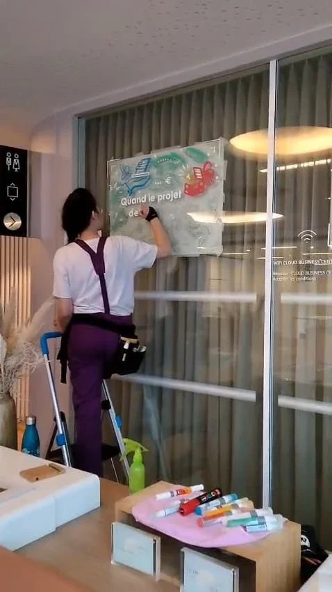 Sandrine Daniel peint une vitrine sur son escabeau lors de la réalisation des décors des Trophées de l'innovation de l'Apec