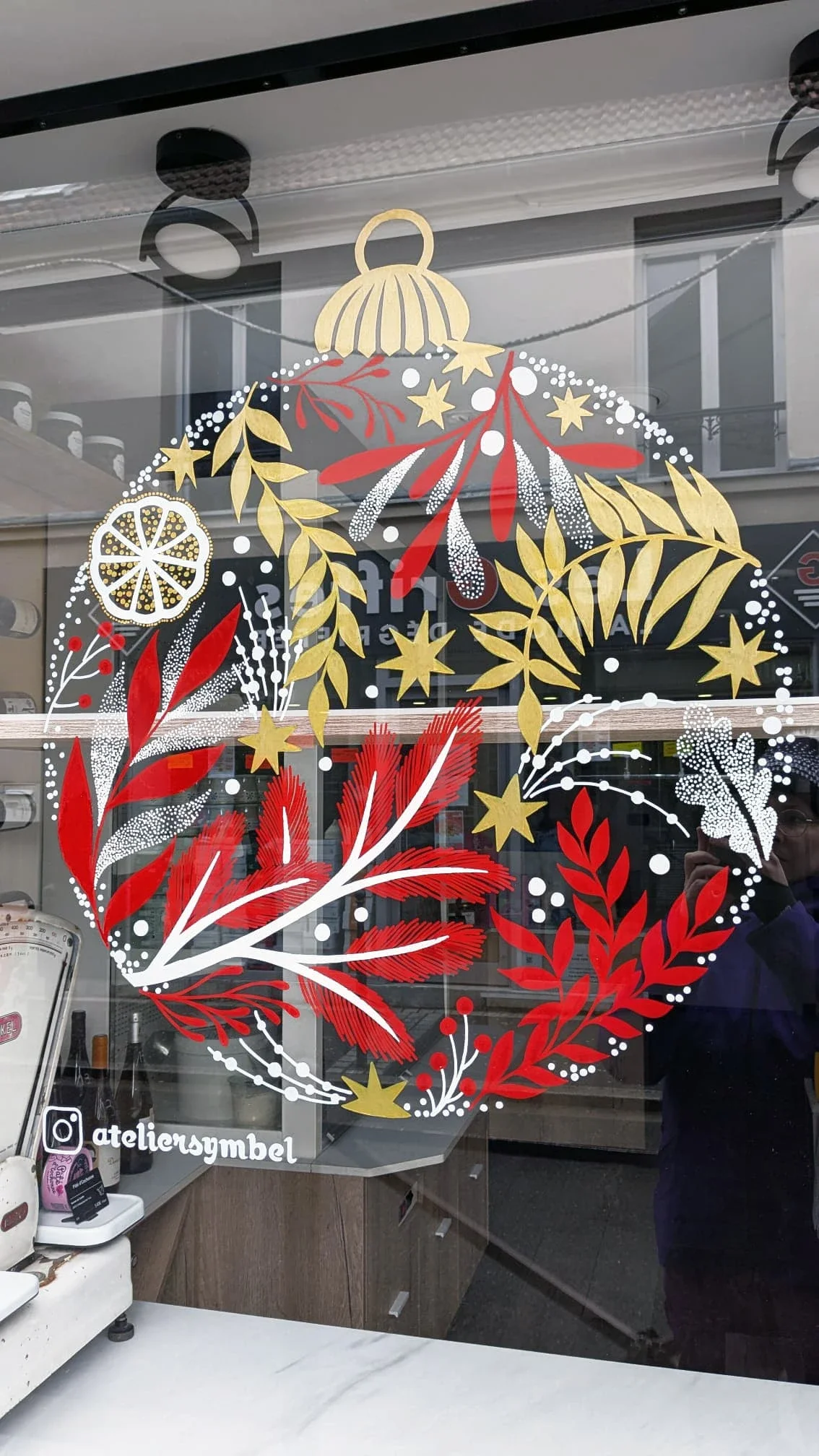 Gros plan sur une boule de Noël peinte à la main avec feuillages, tranche d'agrume, coloris blanc, rouge et doré, réalisée pour la vitrine de la fromagerie Lallias à Houilles