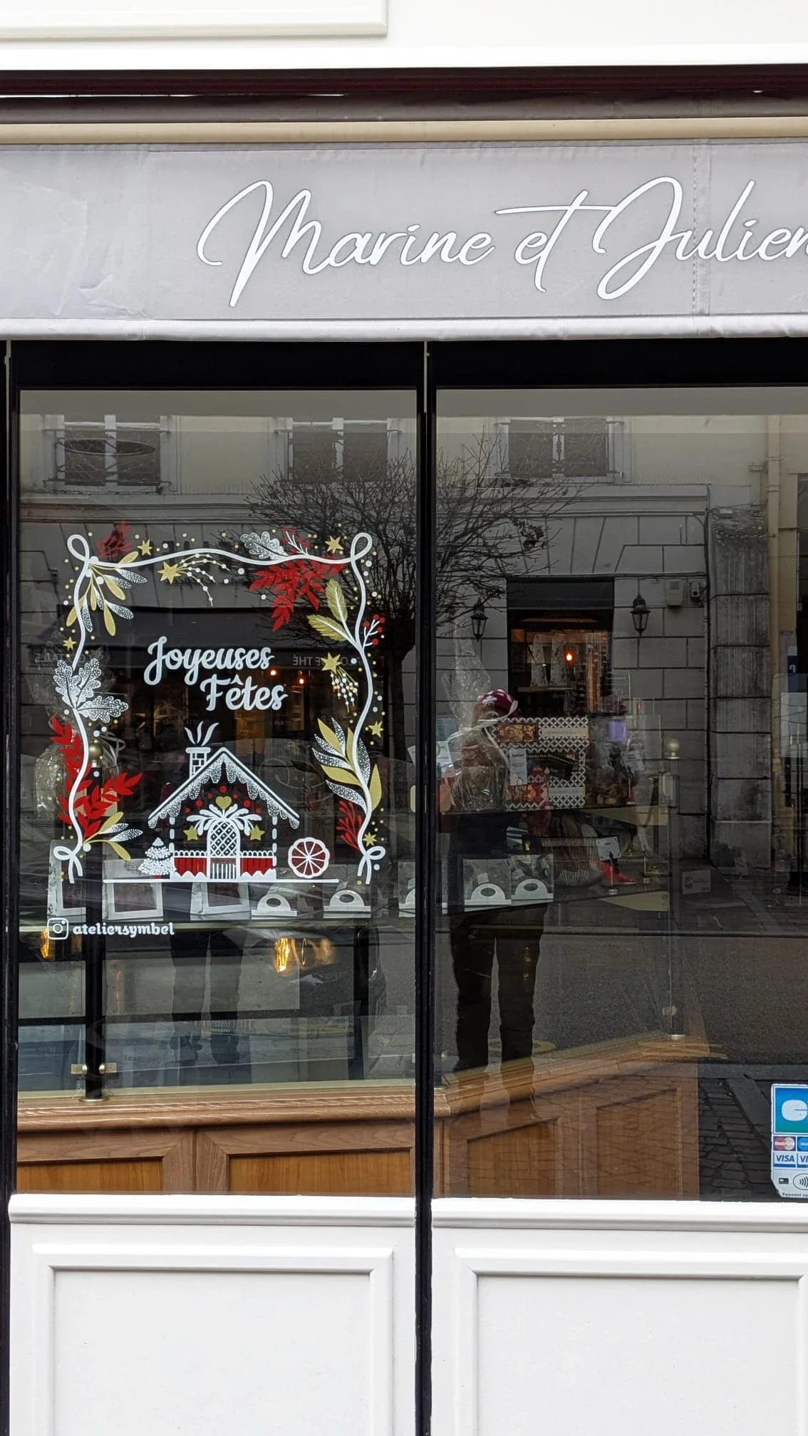 Vue d'ensemble de la peinture sur vitrine de Noël de la boulangerie Duhamel à Saint-Germain-en-Laye, composée d'une frise végétale peinte à la main, d'un lettrage et d'une maison de pain d'épices