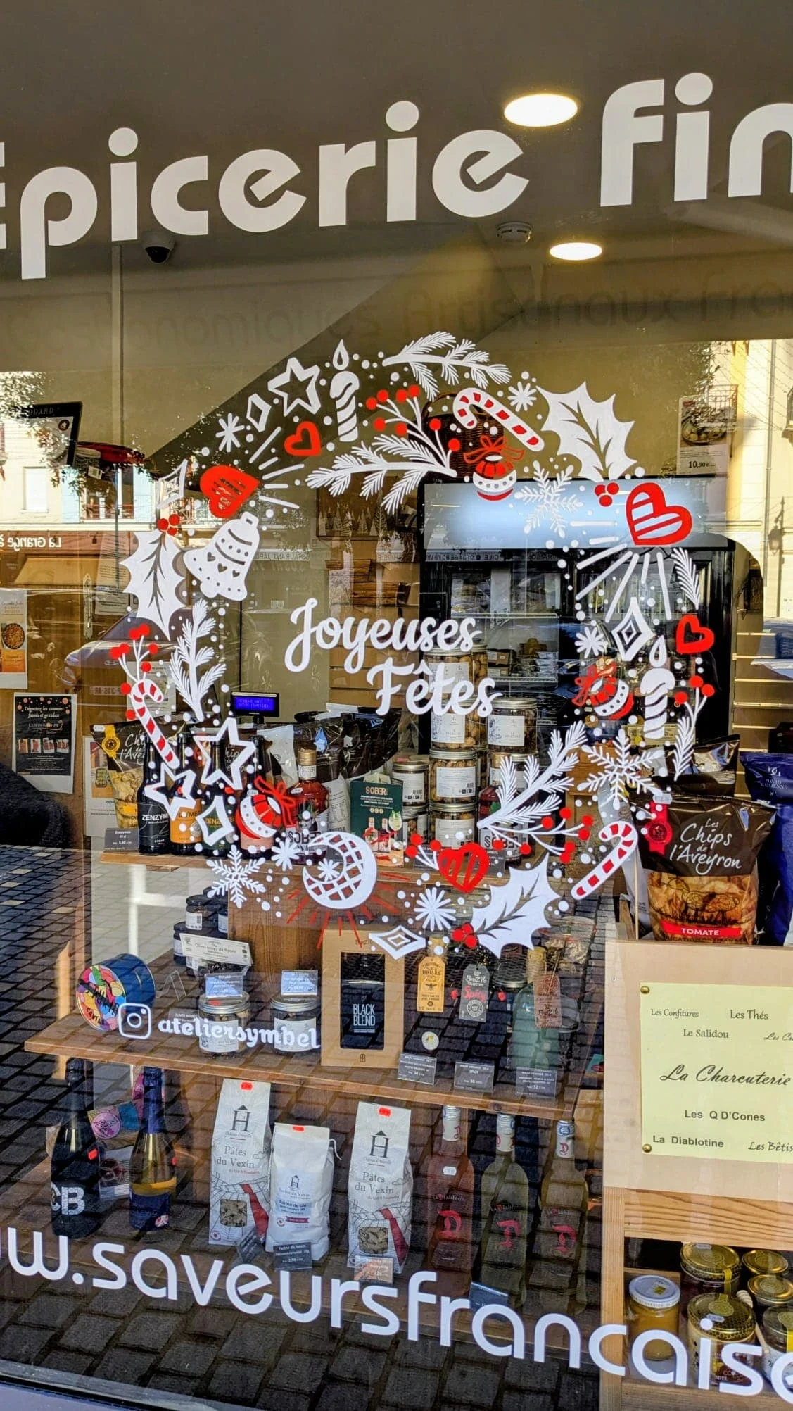 Gros plan sur la couronne Doodle peinte à la main avec houx, cloches, étoiles, baies et branches de pin pour la vitrine de Noël d'uneépicerie fine à Vauréal (95)