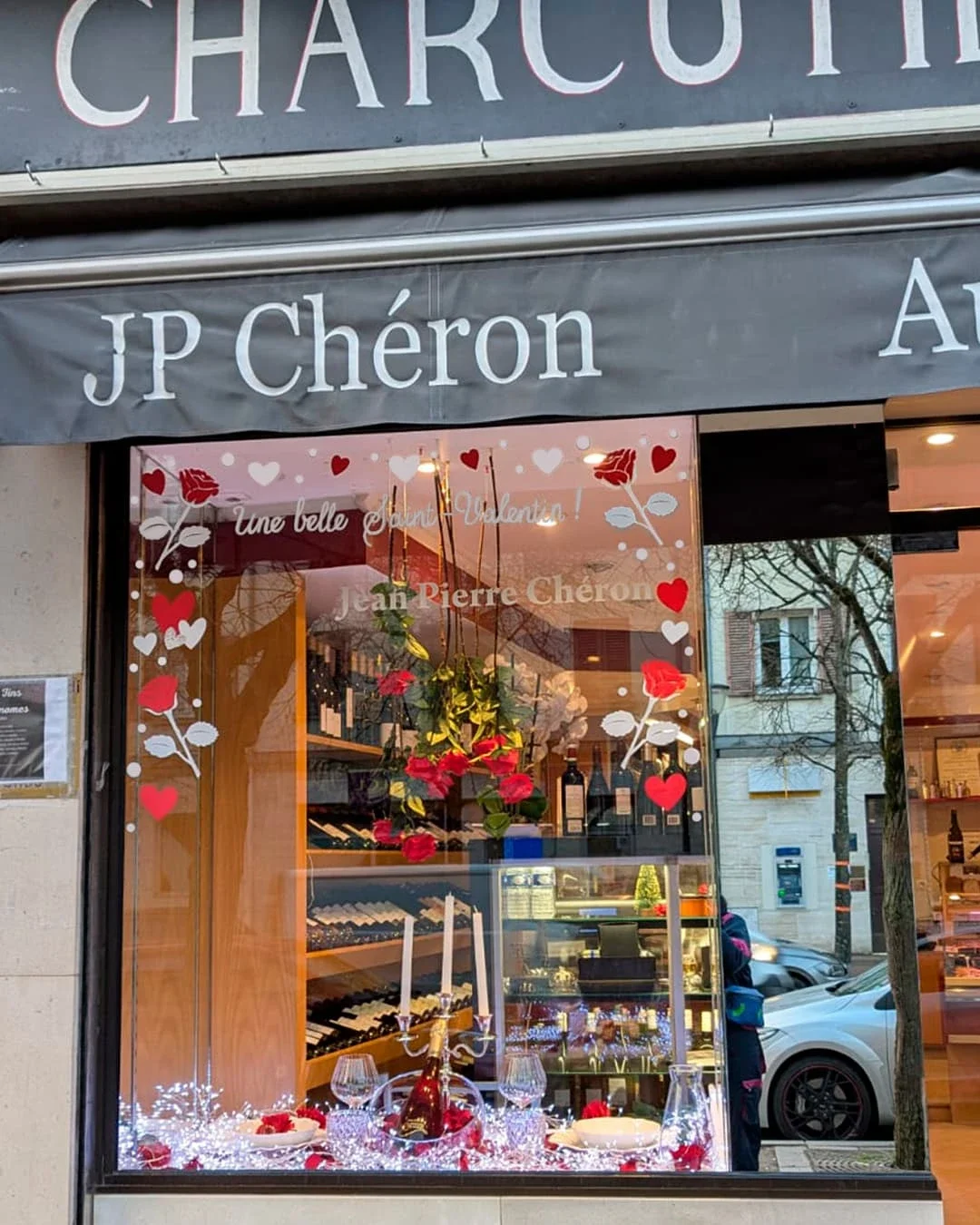 Peinture sur vitrine, thématique Saint-Valentin. Peinture en cours de la vitrine de gauche. Frise décorative avec des roses et des cœurs. Coloris rouge et blanc. Devanture du traiteur JP Chéron à Croissy-sur-Seine (78)