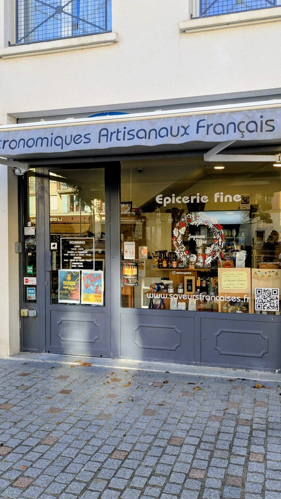 Façade de l'épicerie Saveur Française à Vauréal (95) décorée d'une peinture sur vitrine de Noël représentant une couronne Doodle peinte à la main en rouge et blanc