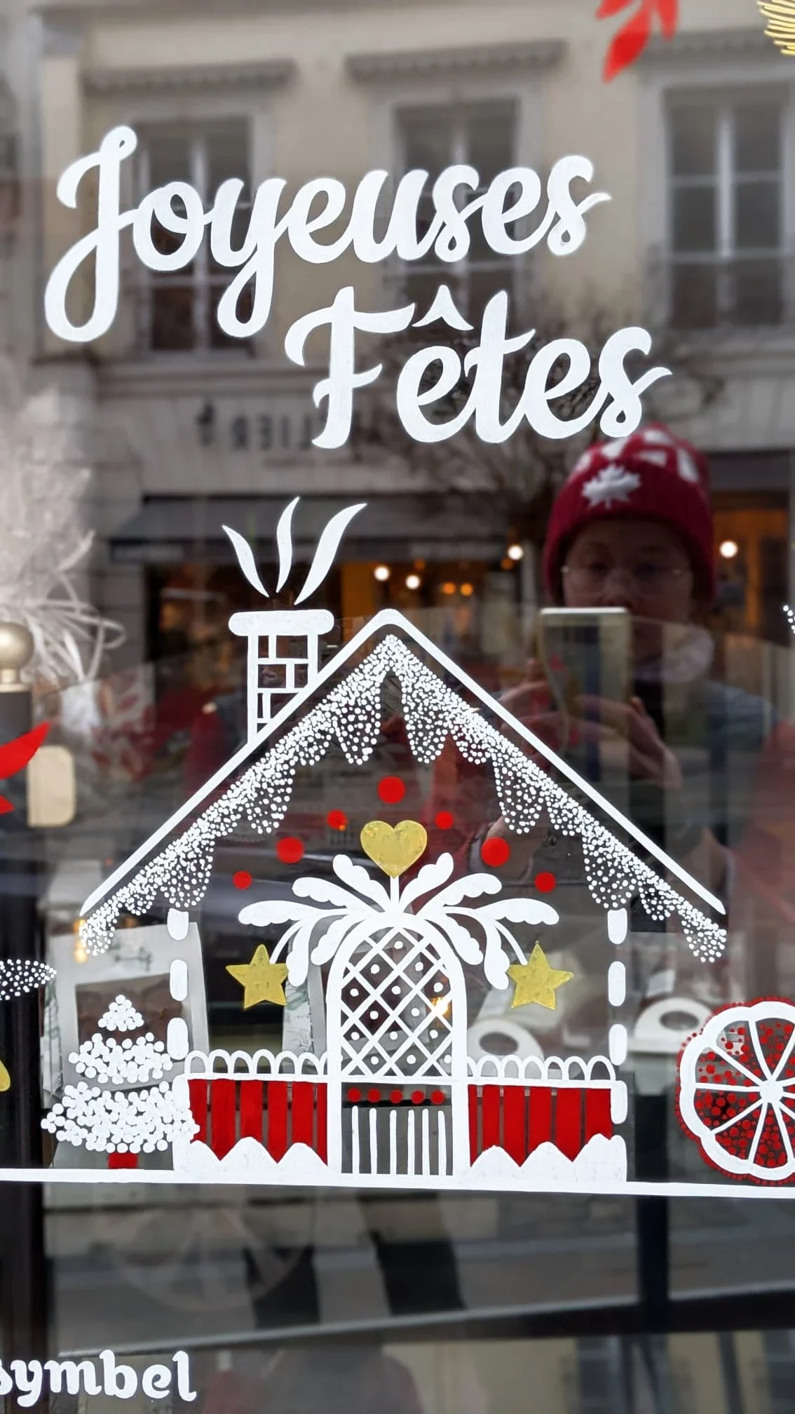 Détail de la peinture sur vitrine de Noël montrant une maison de pain d'épices folklorique et le lettrage peint « Joyeuses fêtes », réalisés à la main