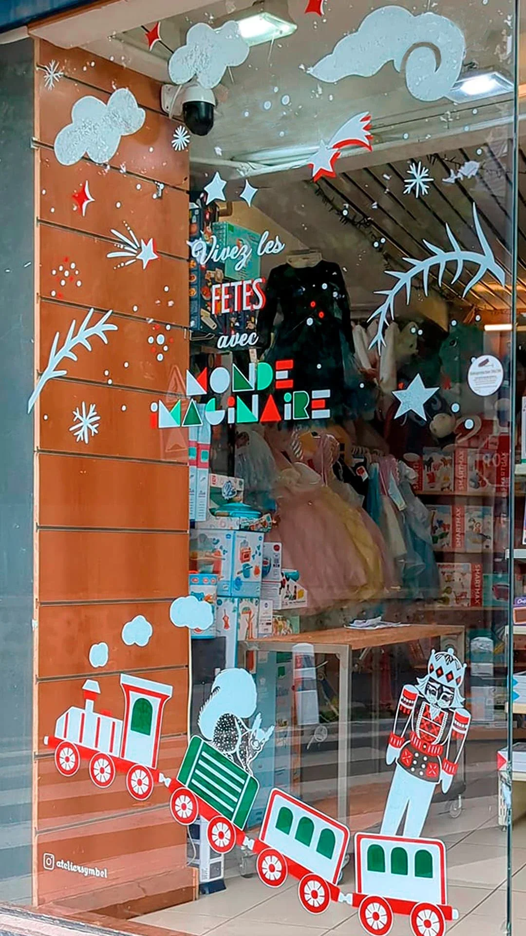 Peinture sur vitrine de Noël sur-mesure pour une boutique de jouets à Houilles (78), avec lettrage et illustrations : branches, étoiles, train d'autrefois, casse-noisette et écureuils
