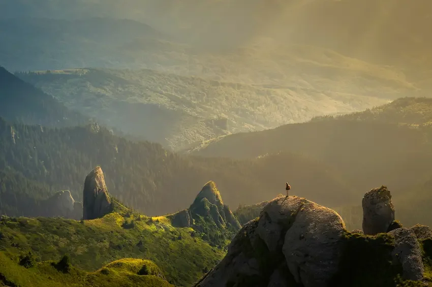 A person standing on top of a mountain in an idyllic setting surrounded by warm sun