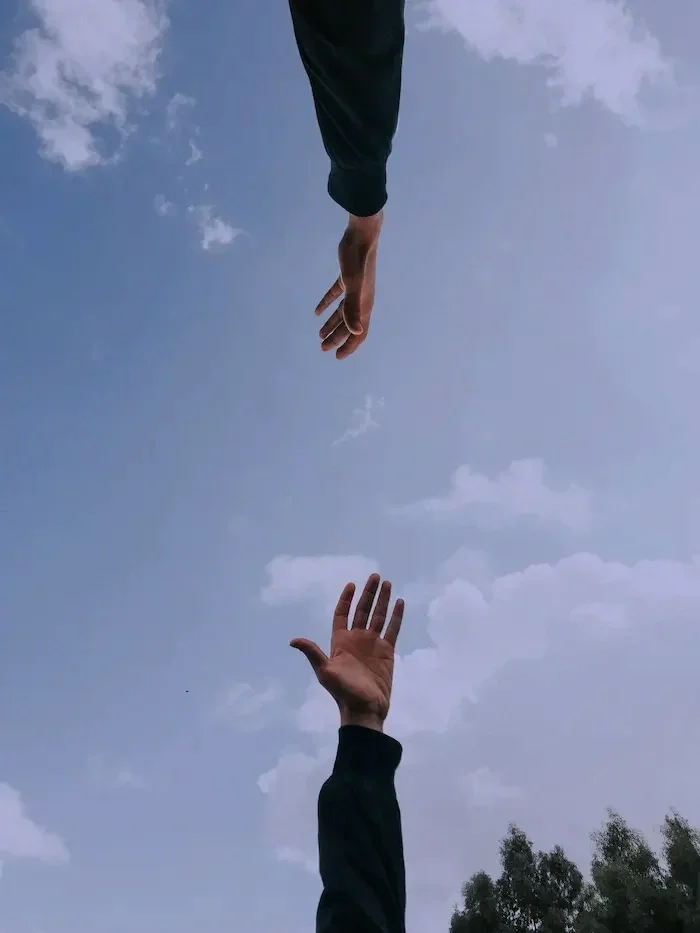 Two hands reaching for each other in a bright, outdoor setting