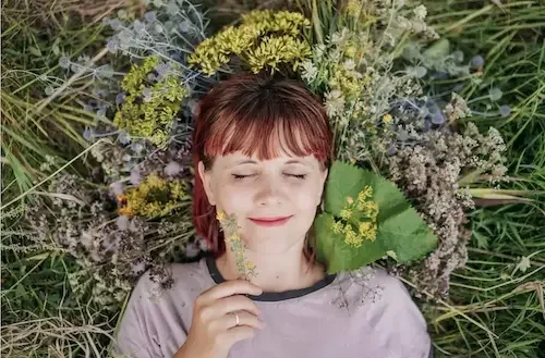 A woman with short red hair lies peacefully in a field with her eyes closed.
