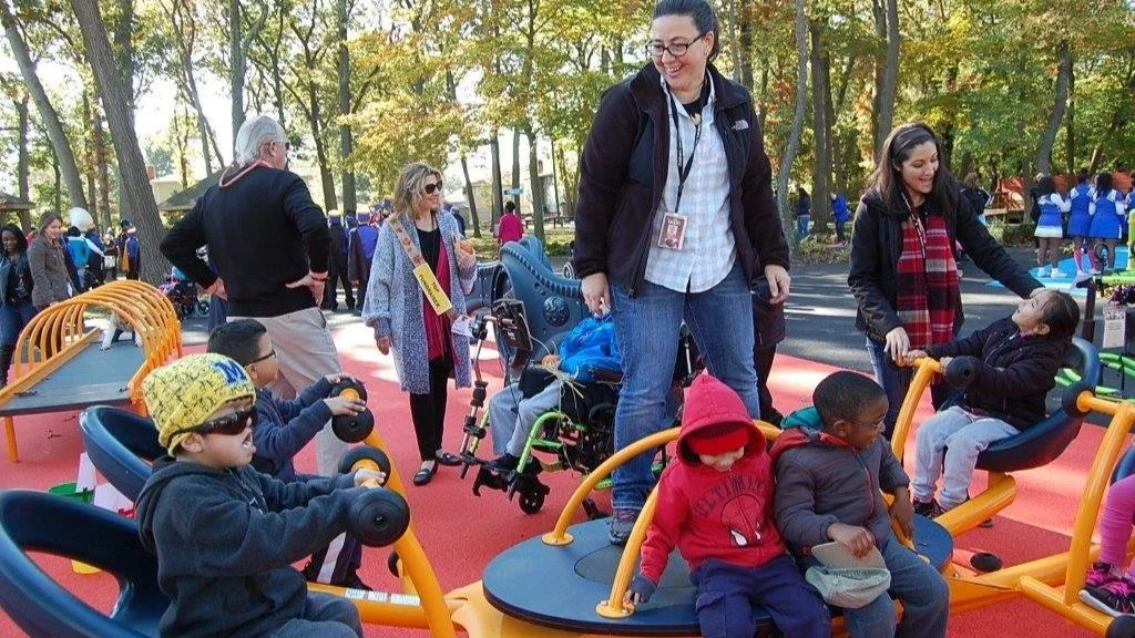 Children and adults enjoying outdoor playground equipment in park on autumn day.