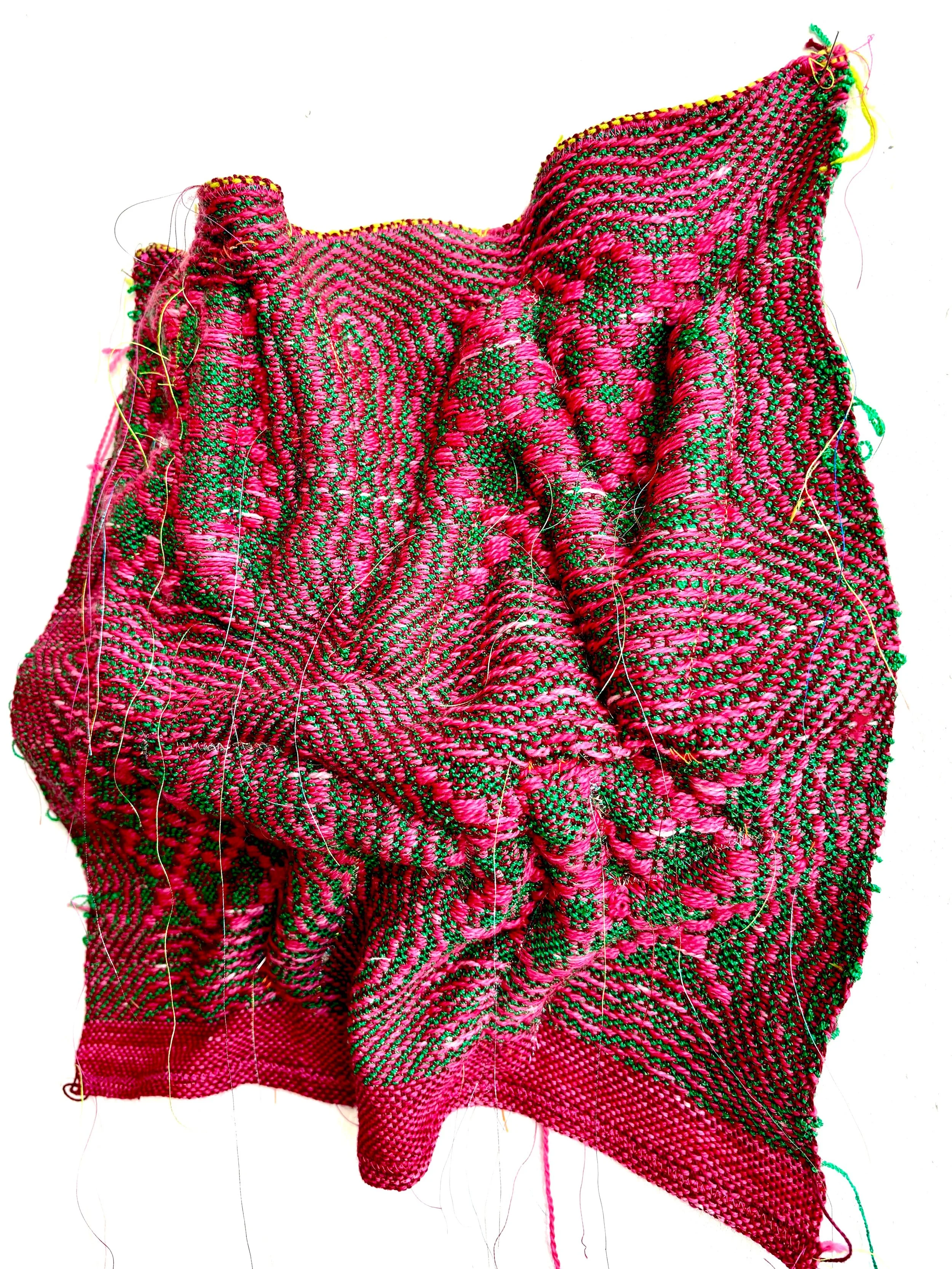 Close-up of a pink and green woven fabric with intricate patterns and some loose threads.