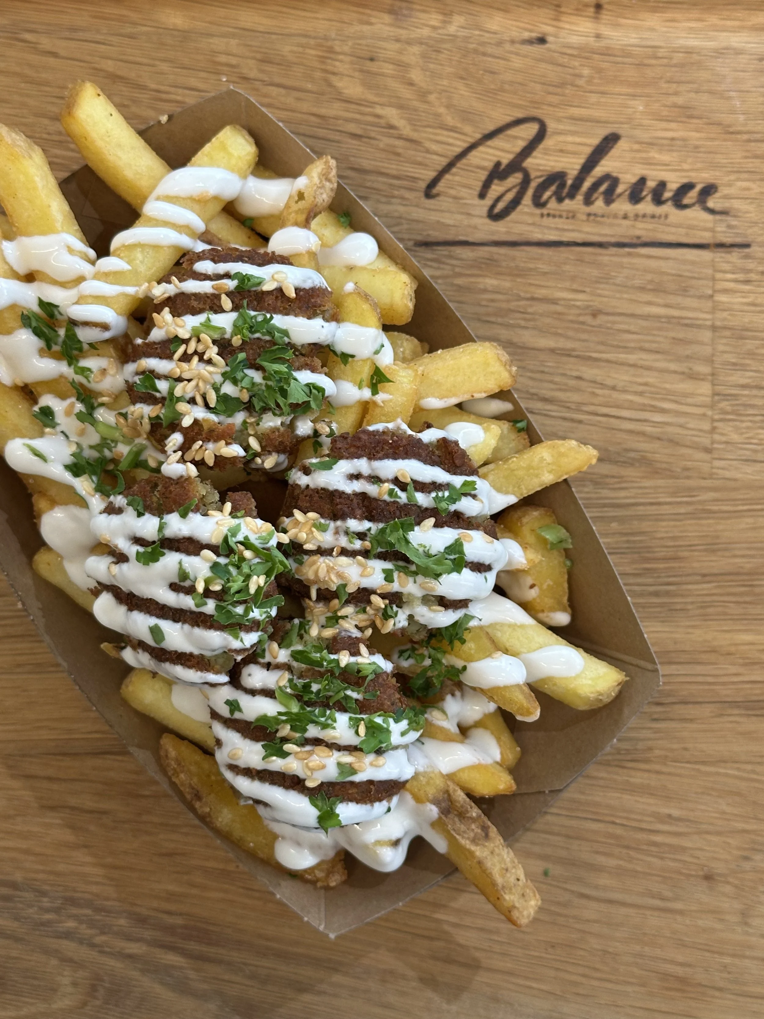 Pommes frites mit Falafel, Soße, gehackten Kräutern und Sesamsamen