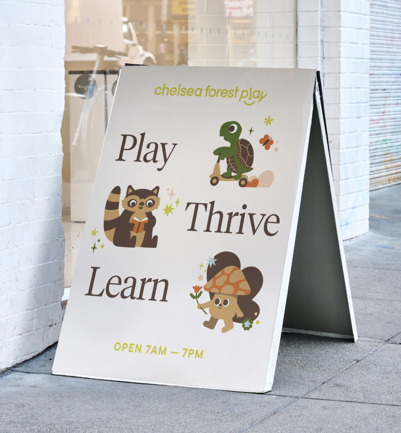 A white sandwich board sign outside a business with the words "chelsea forest play" in lime green, and "Play", "Thrive", and "Learn" in brown, along with cartoon illustrations of a turtle on a scooter, a raccoon reading a book, and a mushroom with a face holding a flower. The bottom states the hours: "OPEN 7AM - 7PM" in yellow.