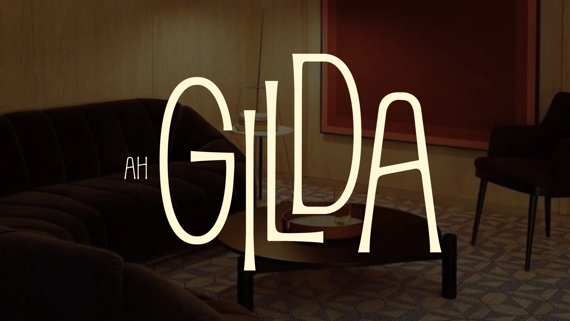 A dimly lit living room with a dark sofa, a side table with a glass of water, a tall backing painting, and a black chair. The words 'AH GILD' are overlaid in large stylized letters.