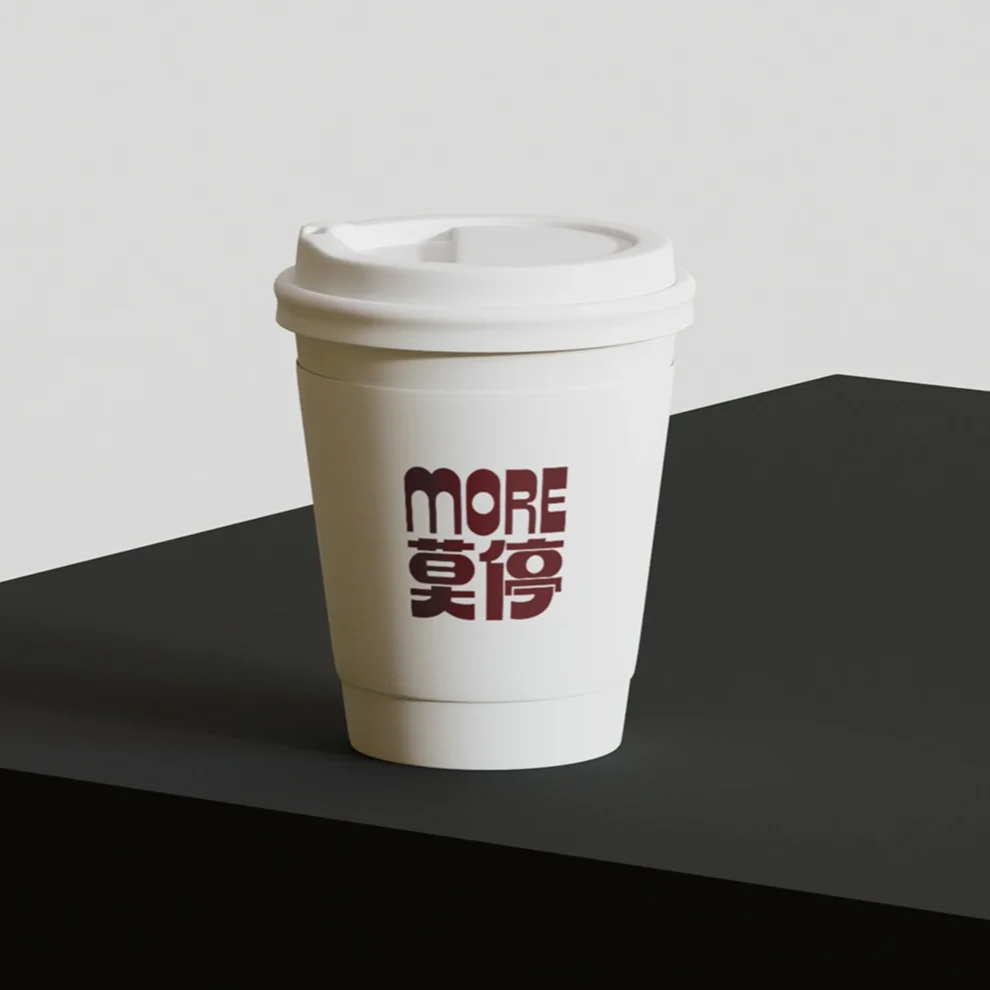 A disposable coffee cup with a white lid and a logo that reads 'MORE' above Chinese characters, placed on a black surface against a plain white background.