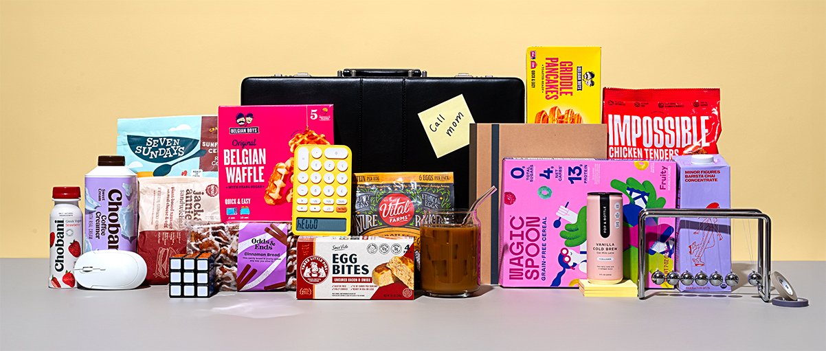 A variety of snacks, candies, and small items arranged on a table, including chocolate, a Rubik's cube, a calculator, a small box, a jar, and a Newton's Cradle.