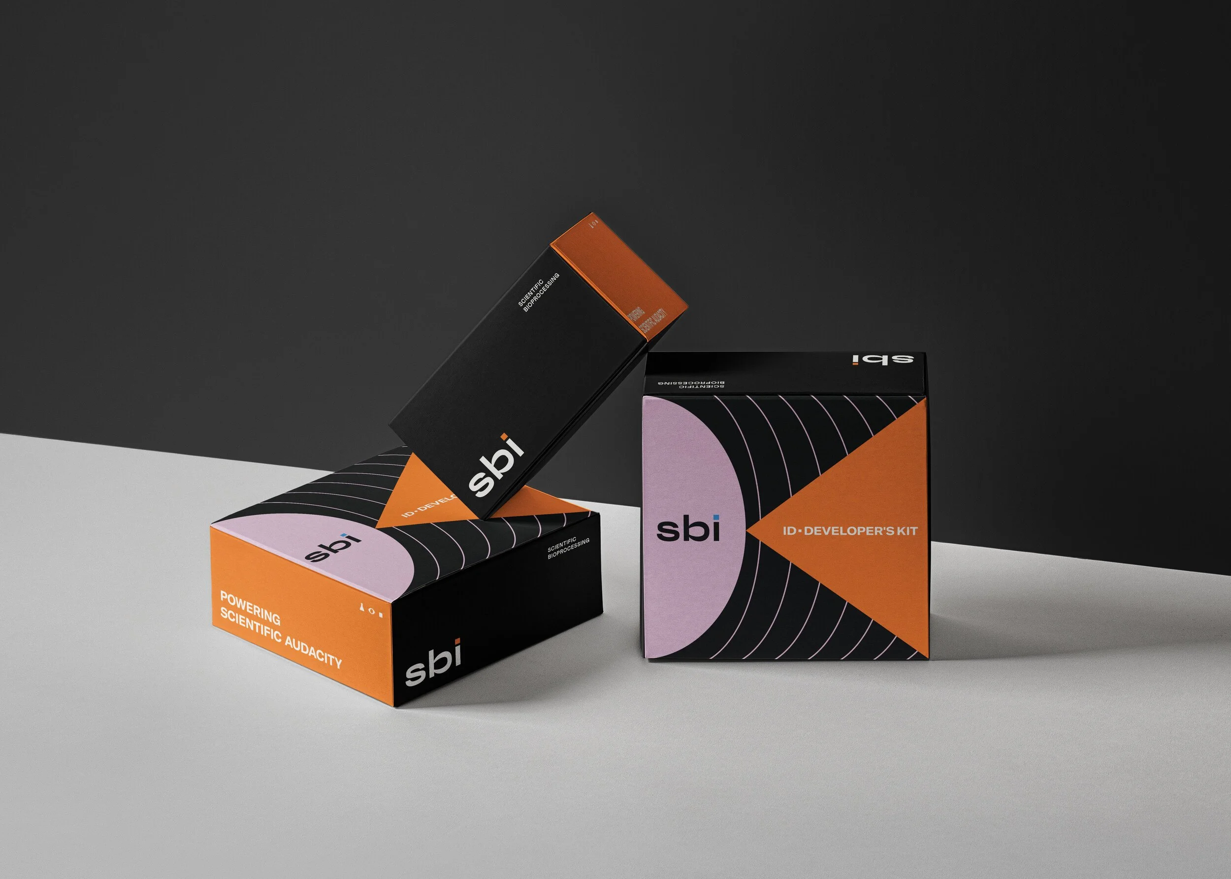 Three black boxes with orange and purple design elements, labeled 'sbi' and 'ID Developer's Kit,' positioned on a split black and white background.