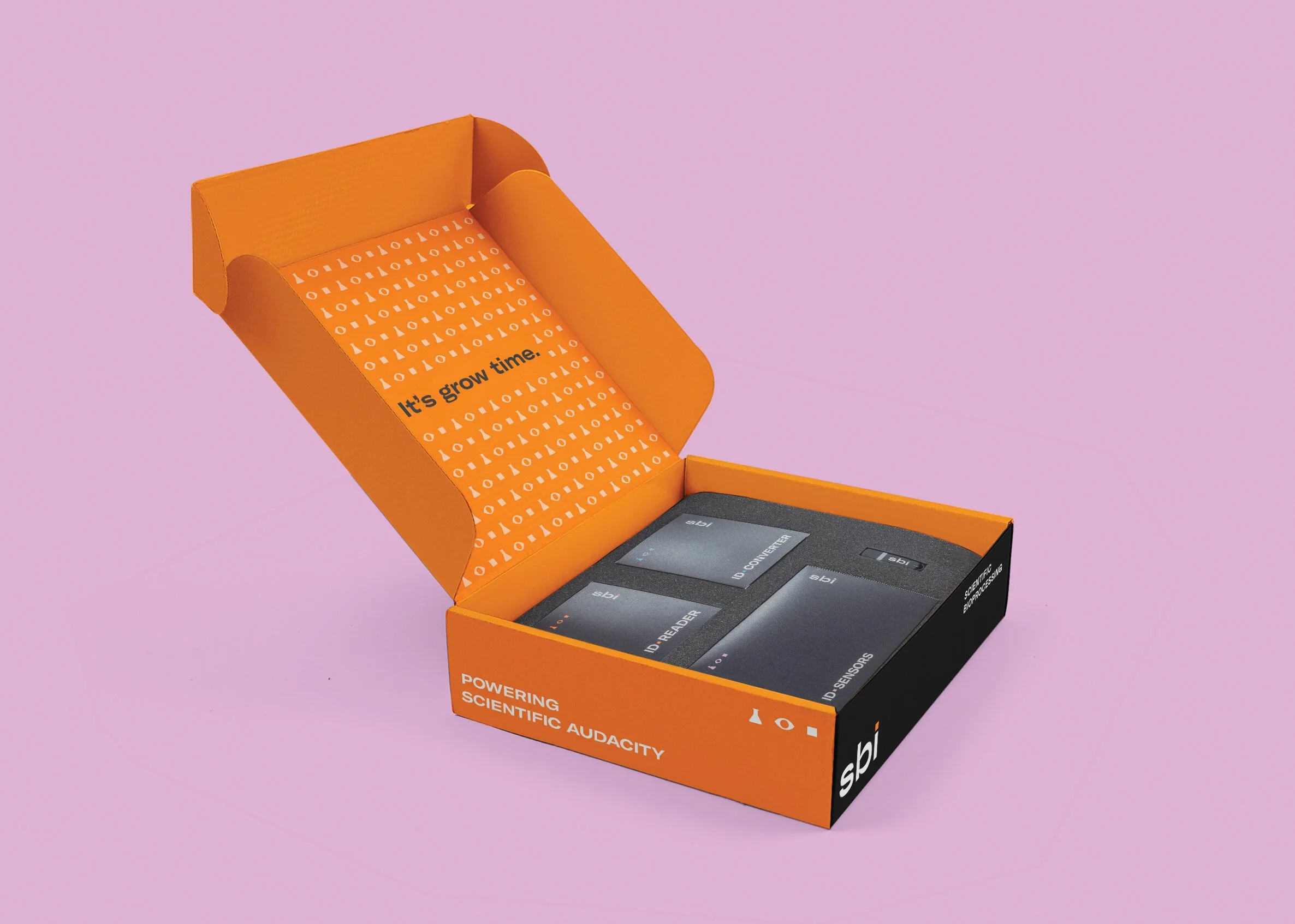 An orange and black box containing scientific electronic components, with the inside lid saying "It's grow time." The box is on a pink background.