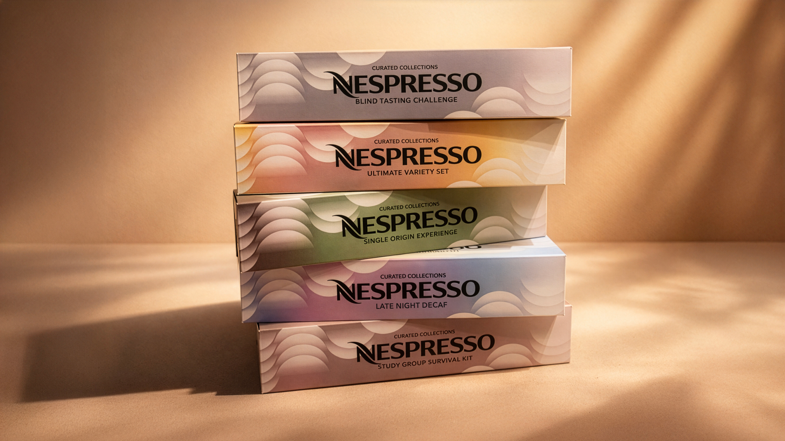 Stack of five Nespresso coffee boxes in pastel colors, arranged on a beige surface with a plain beige background. Each box features the Nespresso logo and the collection name.
