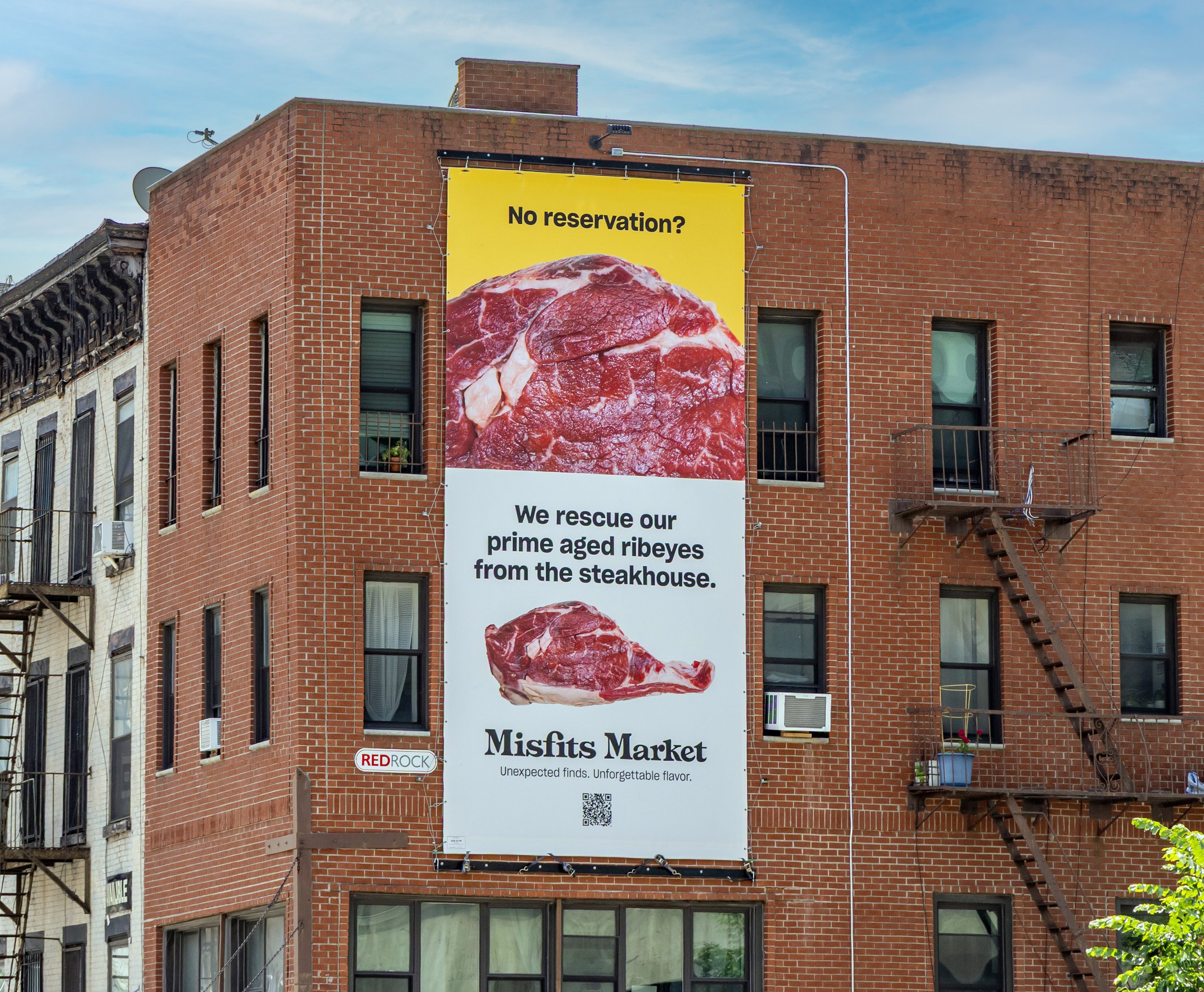 Large vertical outdoor advertisement on a brick building showing images of prime aged ribeye steaks with text about rescuing prime aged ribeyes from a steakhouse, advertising Misfits Market.