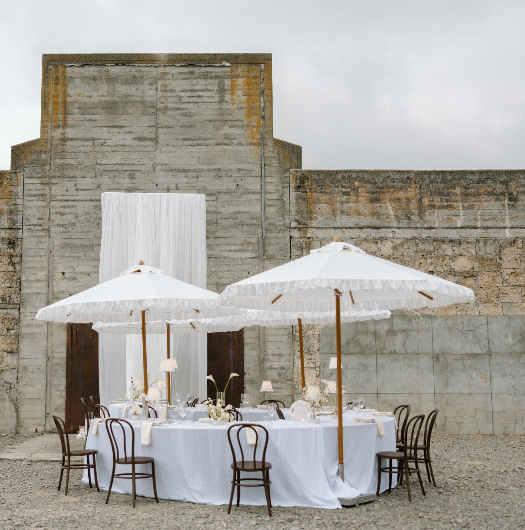 Walnut Bentwood chairs around a serpentine table under white frill umbrellas – Loula Event Hire