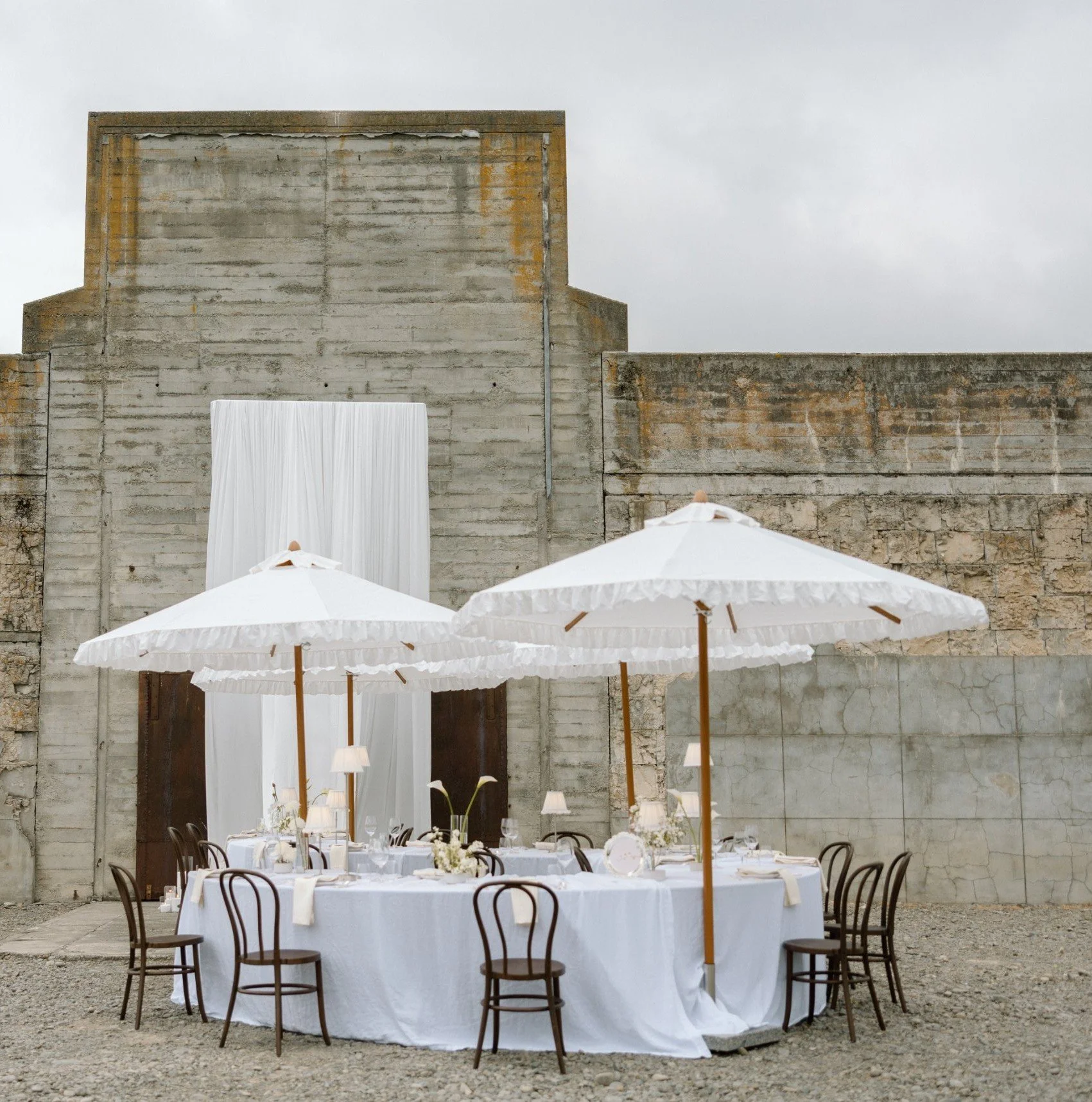 White frill umbrellas over a serpentine table with walnut Bentwood chairs – Loula Event Hire