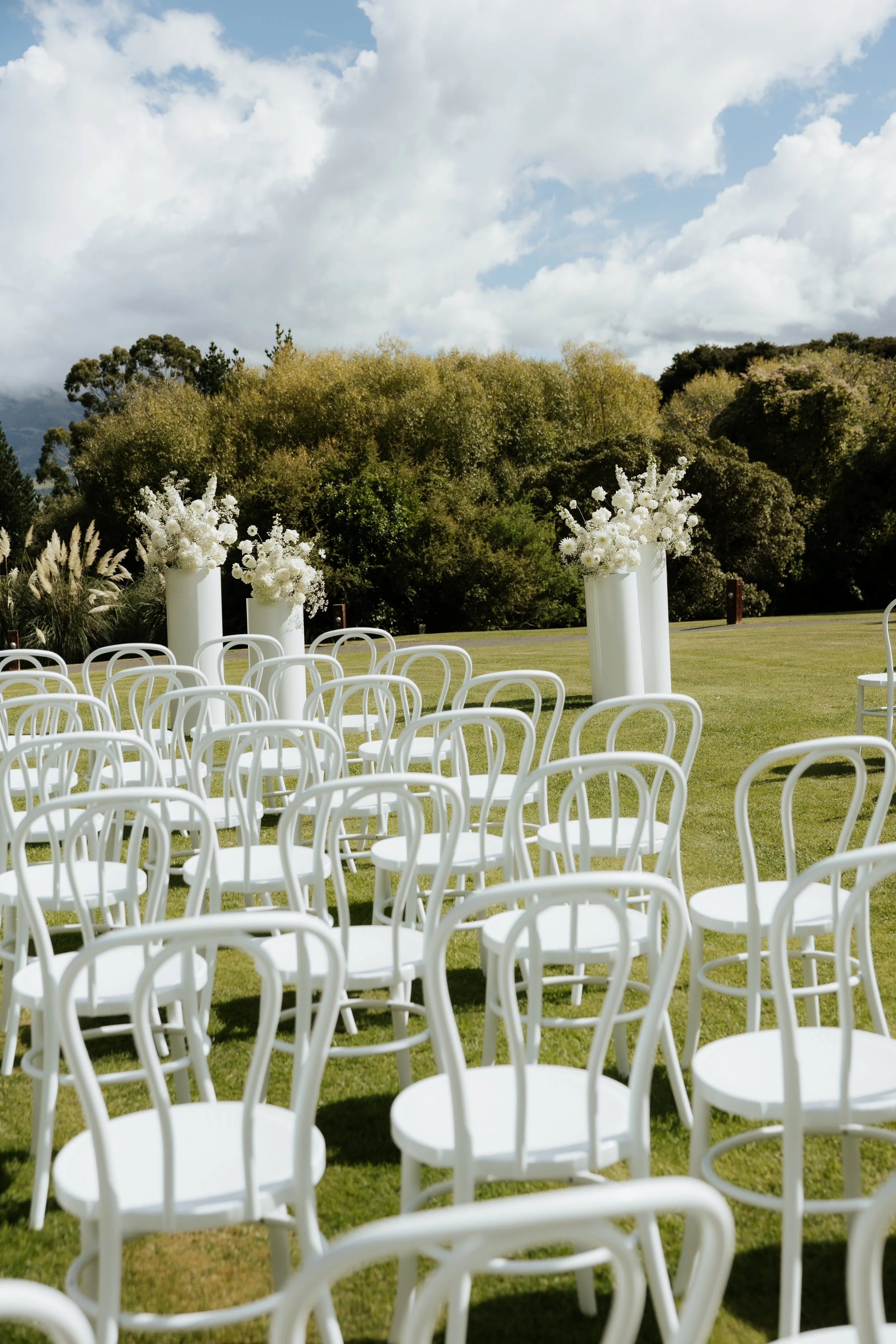 Rows of white Bentwood chairs for the ceremony at Grace & Callum's wedding in Akaroa