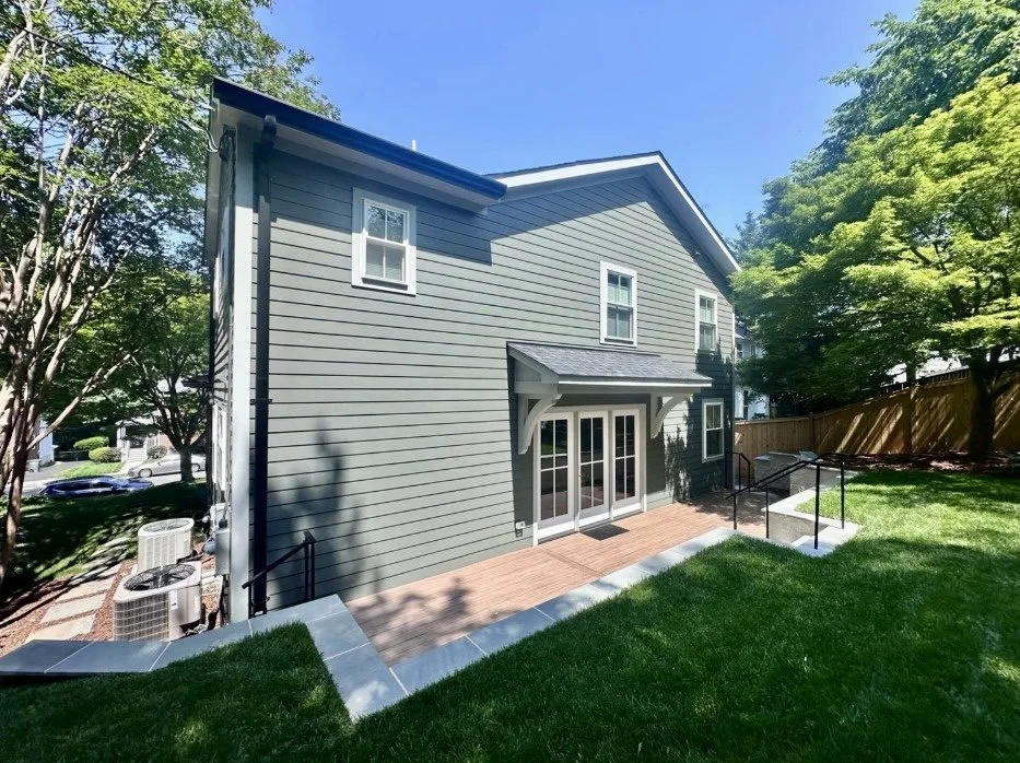 Renovation and Addition of a two-story house with white trim, featuring a small wooden deck with glass sliding doors and a retaining wall in Arlington, VA.