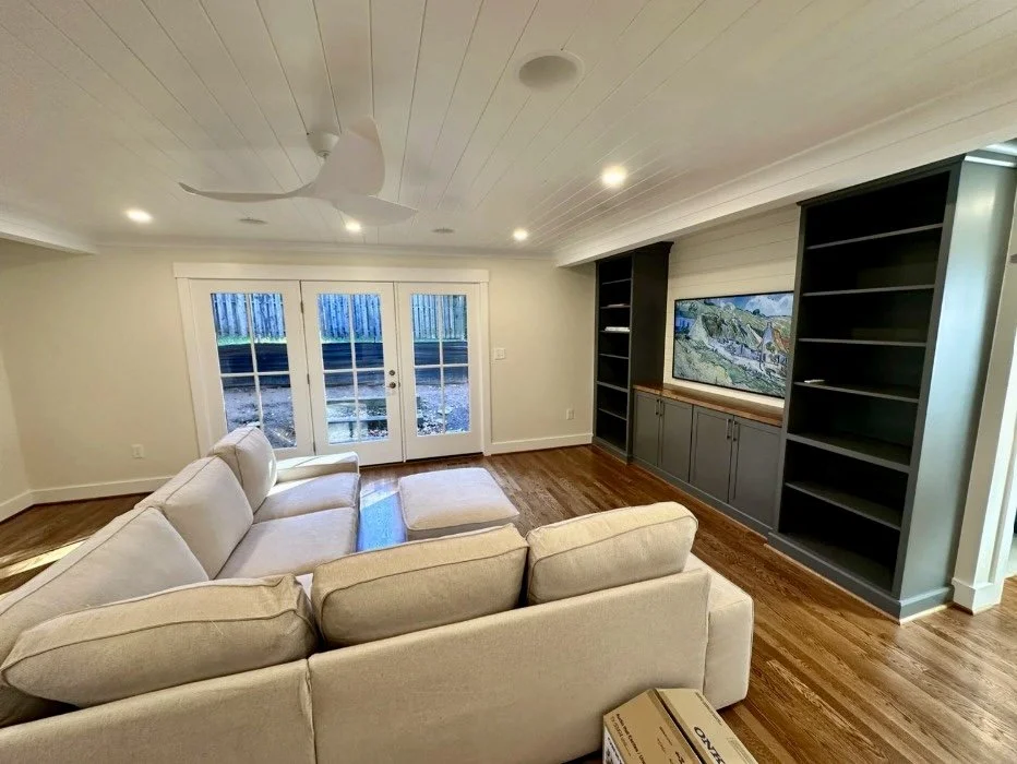 Renovation and Addition of a living room with beige sectional sofa, hardwood floors, built-in gray bookcase and media center, double glass doors leading outside, white ceiling with recessed lighting and a ceiling fan in Arlington VA