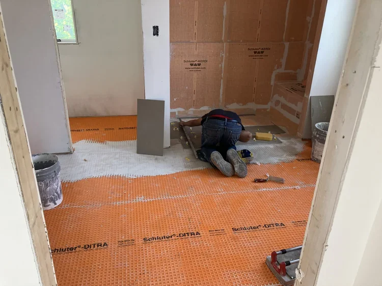 Bathroom floor installation showing orange Schluter-Ditra waterproofing membrane before tiling in Arlington, VA