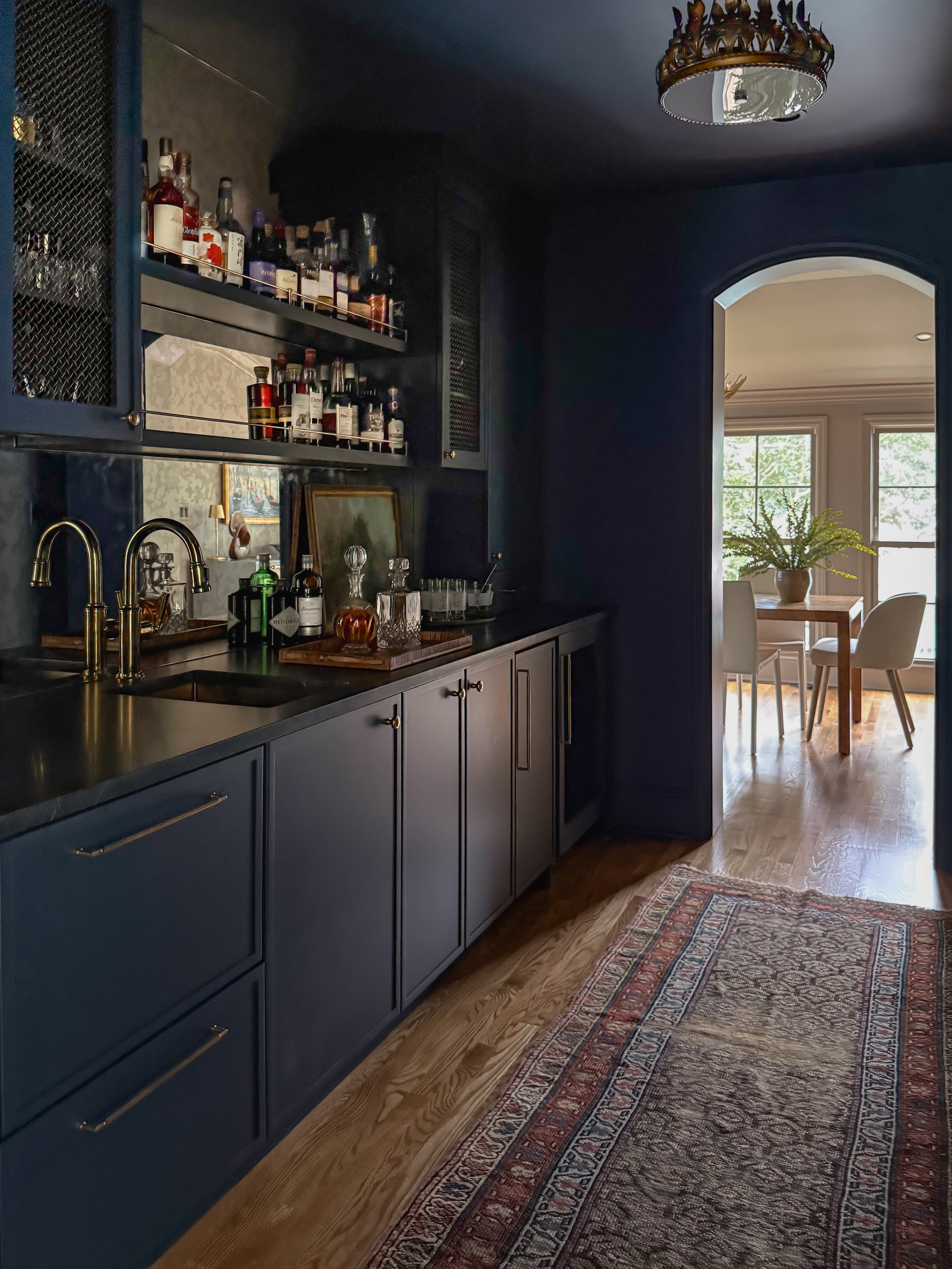Wet bar with custom blue cabinets, antique mirror backsplash, with open shelves and gold hardware finishes.