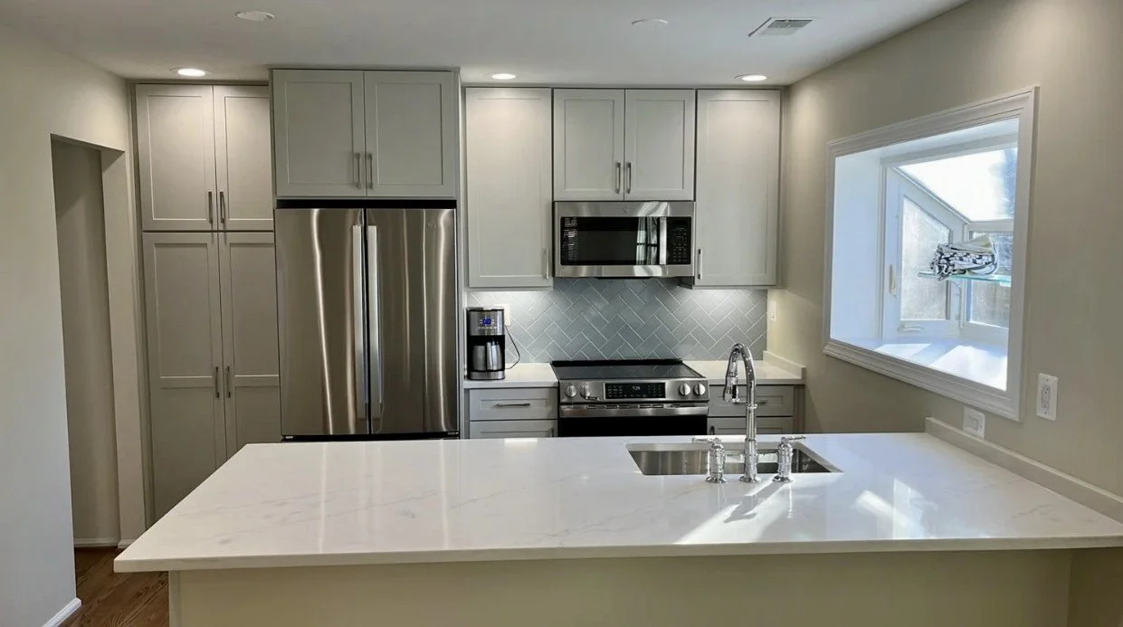 Modern kitchen with white marble countertops, stainless steel appliances, gray cabinets, and a large window.