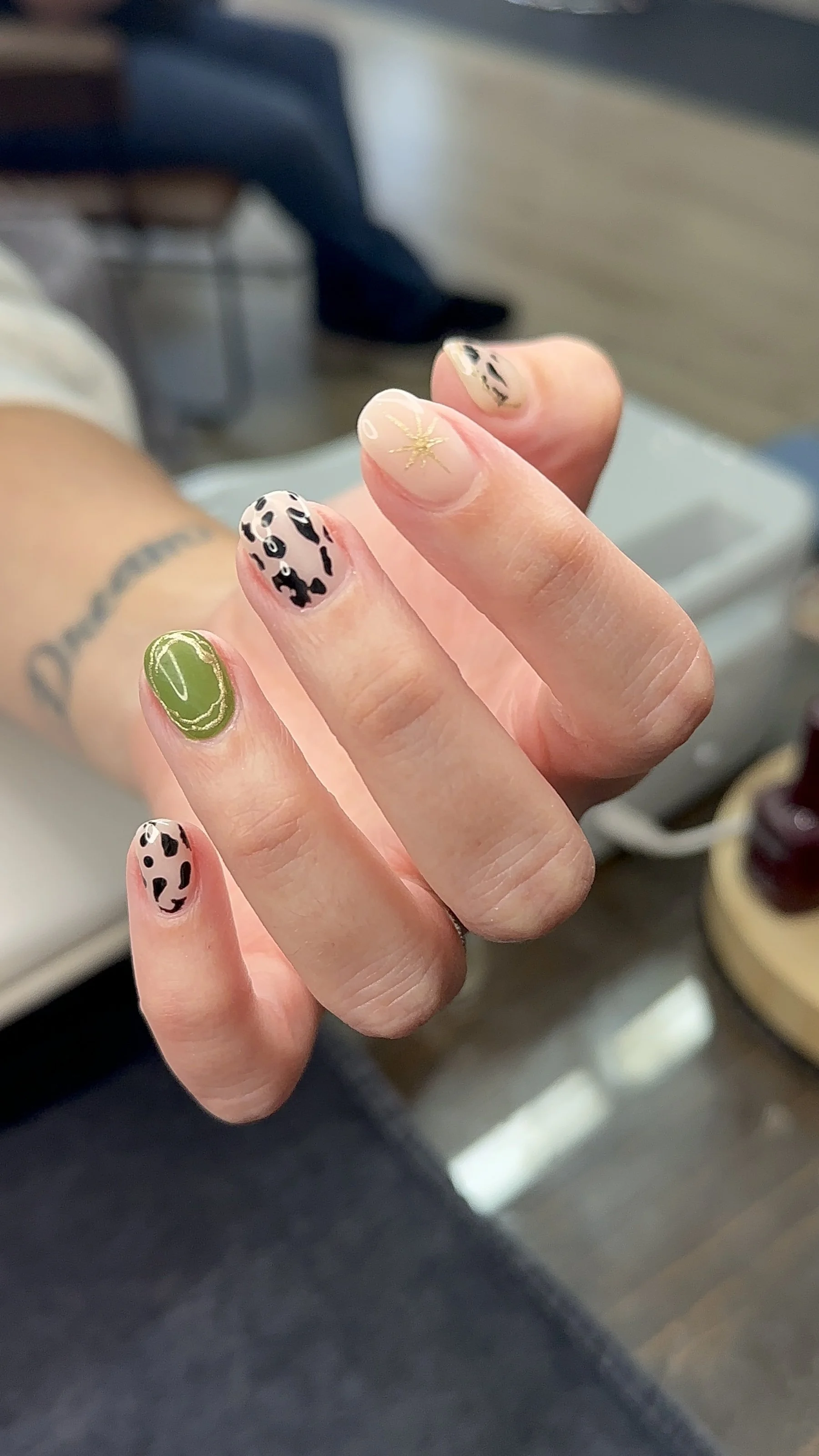 Close-up of a person's hand showing nails decorated with animal print design, a gold glitter star, and a green and white pattern.