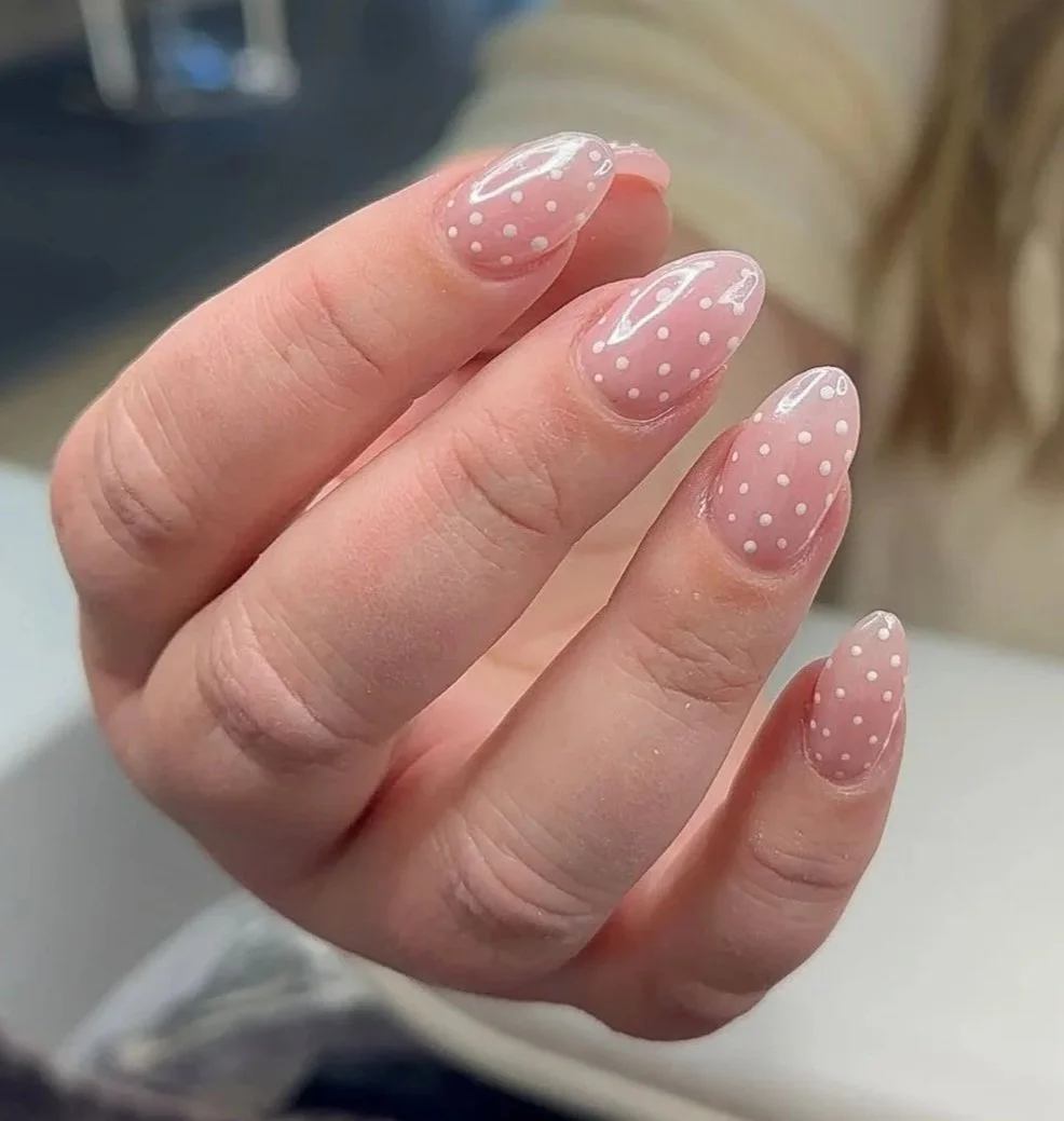 Close-up of a hand with manicured nails painted in a light pink color with white polka dots, nail art design.