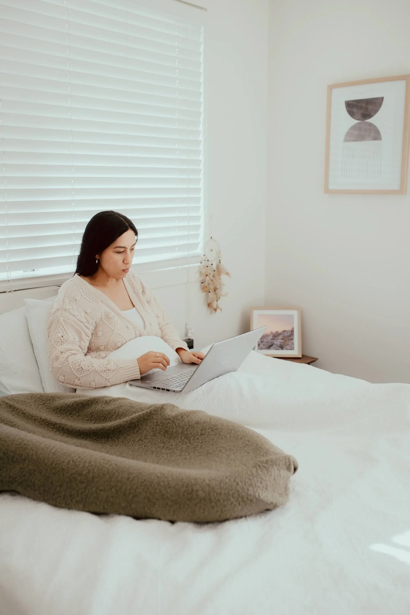 pregnant woman sitting up in bed with laptop open
