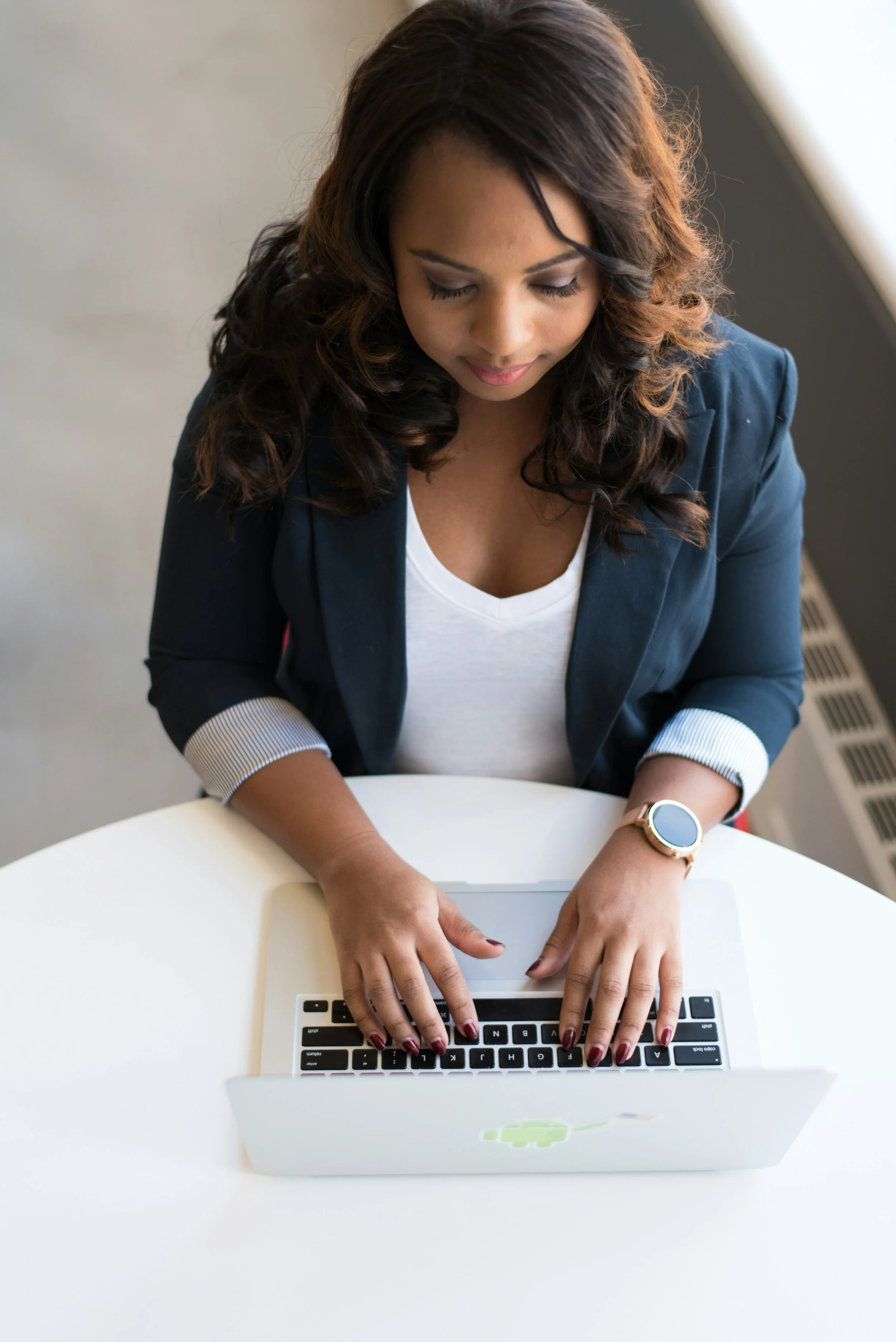 Woman with long dark hair and mahogany skin photographed from the front while looking down and working on her laptop
